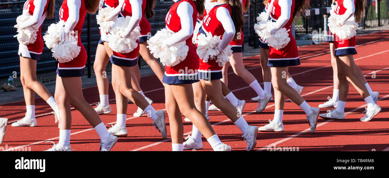 High school cheerleaders en rouge, blanc et bleu pour acclamer les fans dans les gradins pendant un match de football des retrouvailles. Banque D'Images