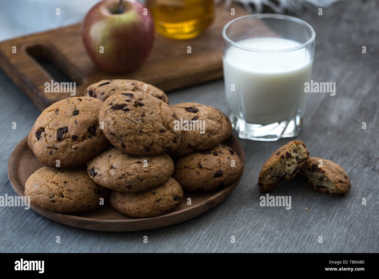 Pile de délicieux cookies aux pépites de chocolat sur une plaque avec un verre de lait sur la table en bois Banque D'Images