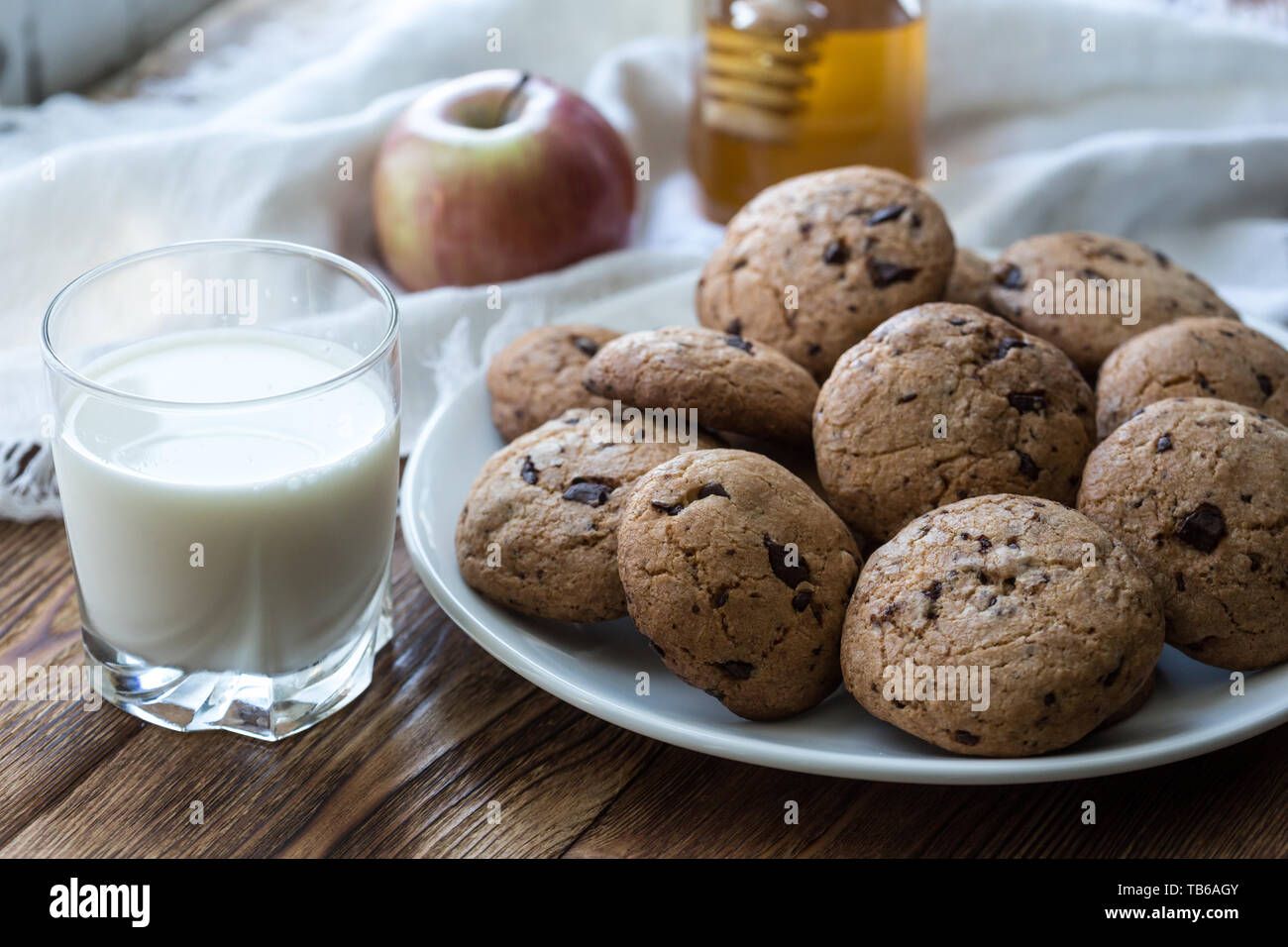 Pile de délicieux cookies aux pépites de chocolat sur une plaque avec un verre de lait sur la table en bois Banque D'Images