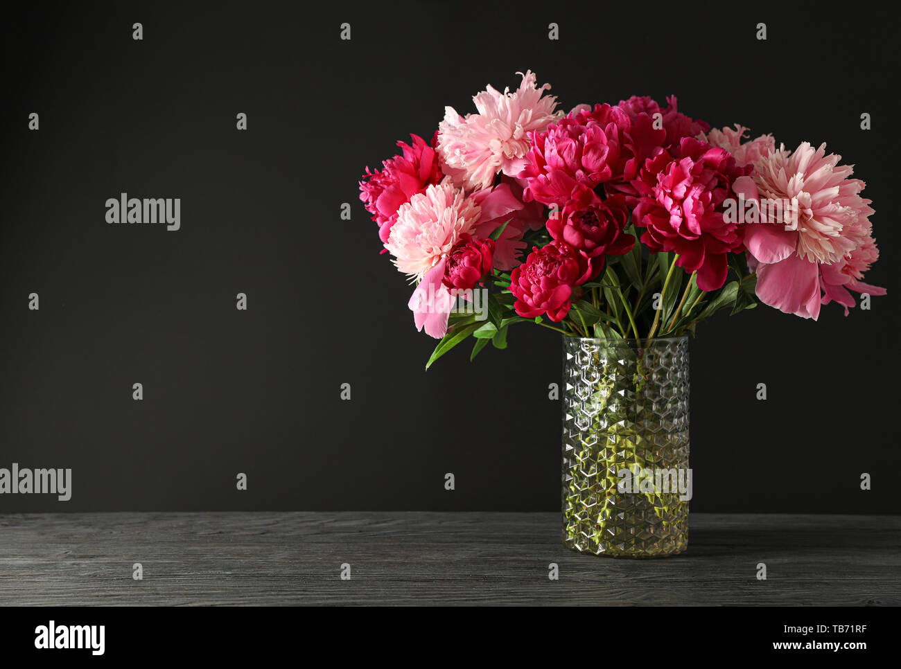 Vase en verre avec bouquet de belles pivoines sur table en bois sur fond noir, de l'espace pour le texte Banque D'Images