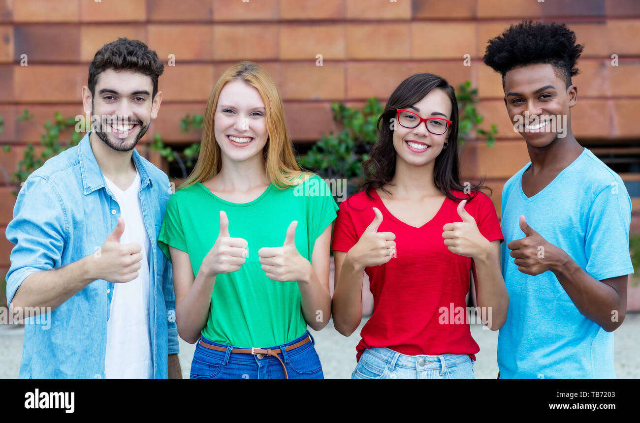 Groupe de quatre jeunes adultes de la génération y showing thumbs piscine en été dans la ville Banque D'Images