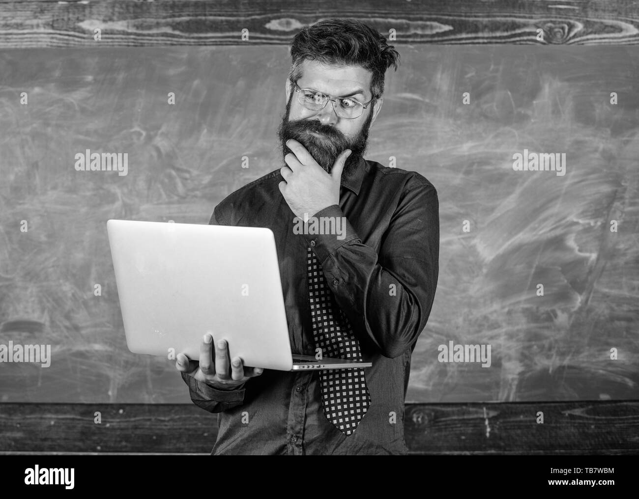 Concept de formation à distance. Surfer sur internet. Professeur Hipster portent des lunettes et cravate est titulaire d'ordinateur portable Internet surf. Homme barbu enseignant avec ordinateur portable moderne tableau internet surf arrière-plan. Banque D'Images