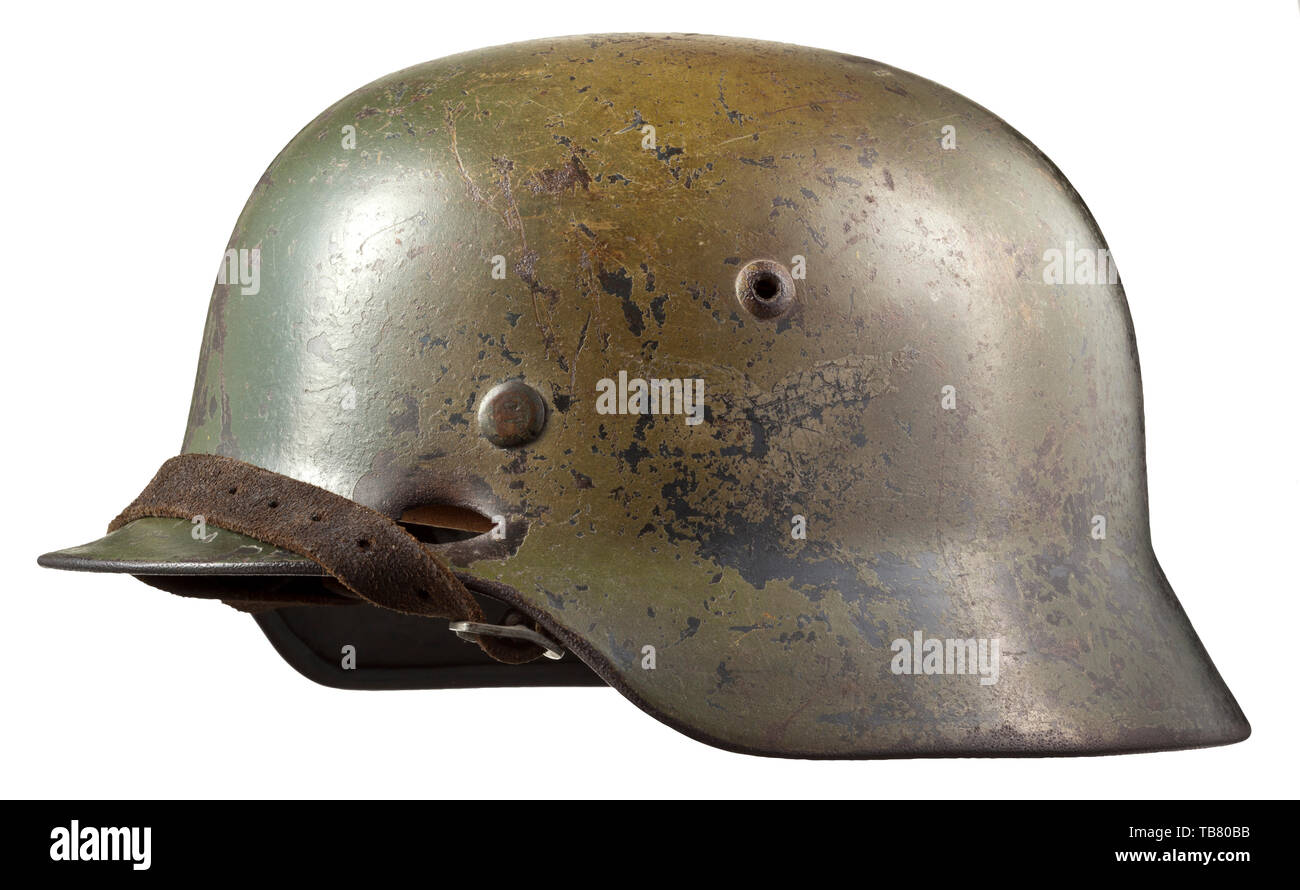 Un casque d'acier M 35 avec de la peinture de camouflage, le crâne gravé sur l'intérieur de 'E64' (Suisse saxonne) Emaillierwerke, petites perforations sur le côté gauche causée par une coquille splinter. Multi-couleur camouflage appliqué sur l'original de la peinture gris-Luftwaffe, les vestiges des deux emblèmes visible sous le camouflage. Complet avec revêtement intérieur et jugulaire historique., historique du 20e siècle, Editorial-Use-seulement Banque D'Images
