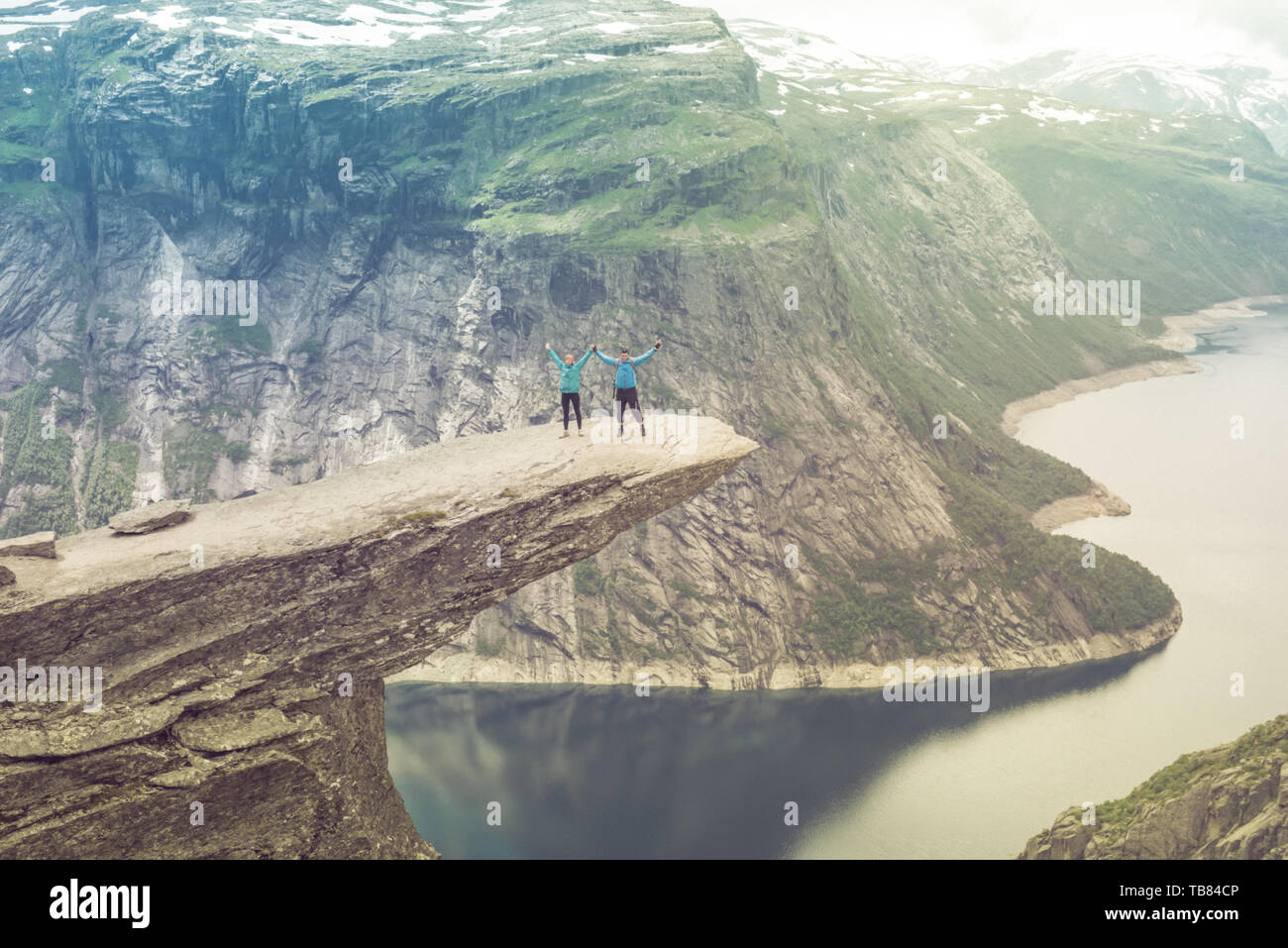 Couple posing sur Trolltunga. La femme et l'homme heureux profiter du magnifique lac et de beau temps en Norvège. Banque D'Images