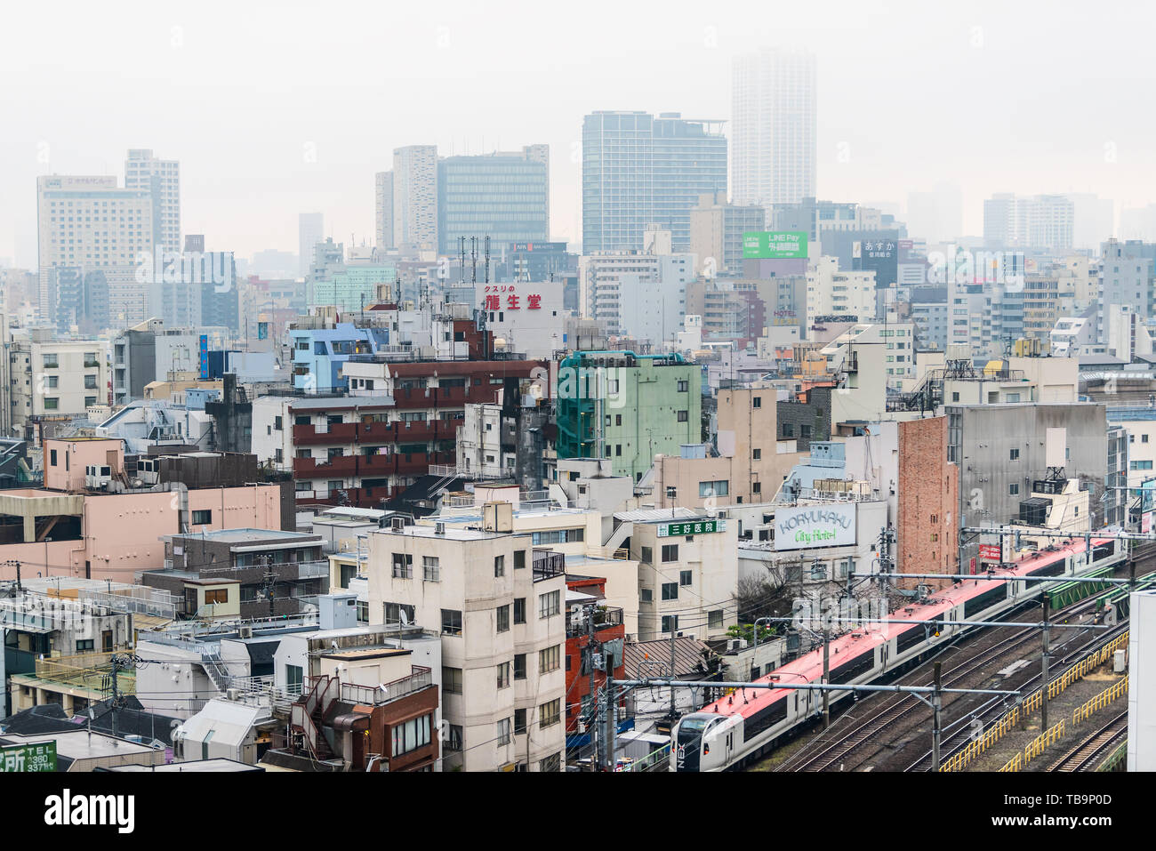 Tokyo, Japon - 30 mars 2019 : Shinjuku cityscape view bâtiments sur brouillard brouillard gris Nuageux Nuageux jour avec de nombreuses maisons et rouge du métro jusqu'à chenilles Banque D'Images