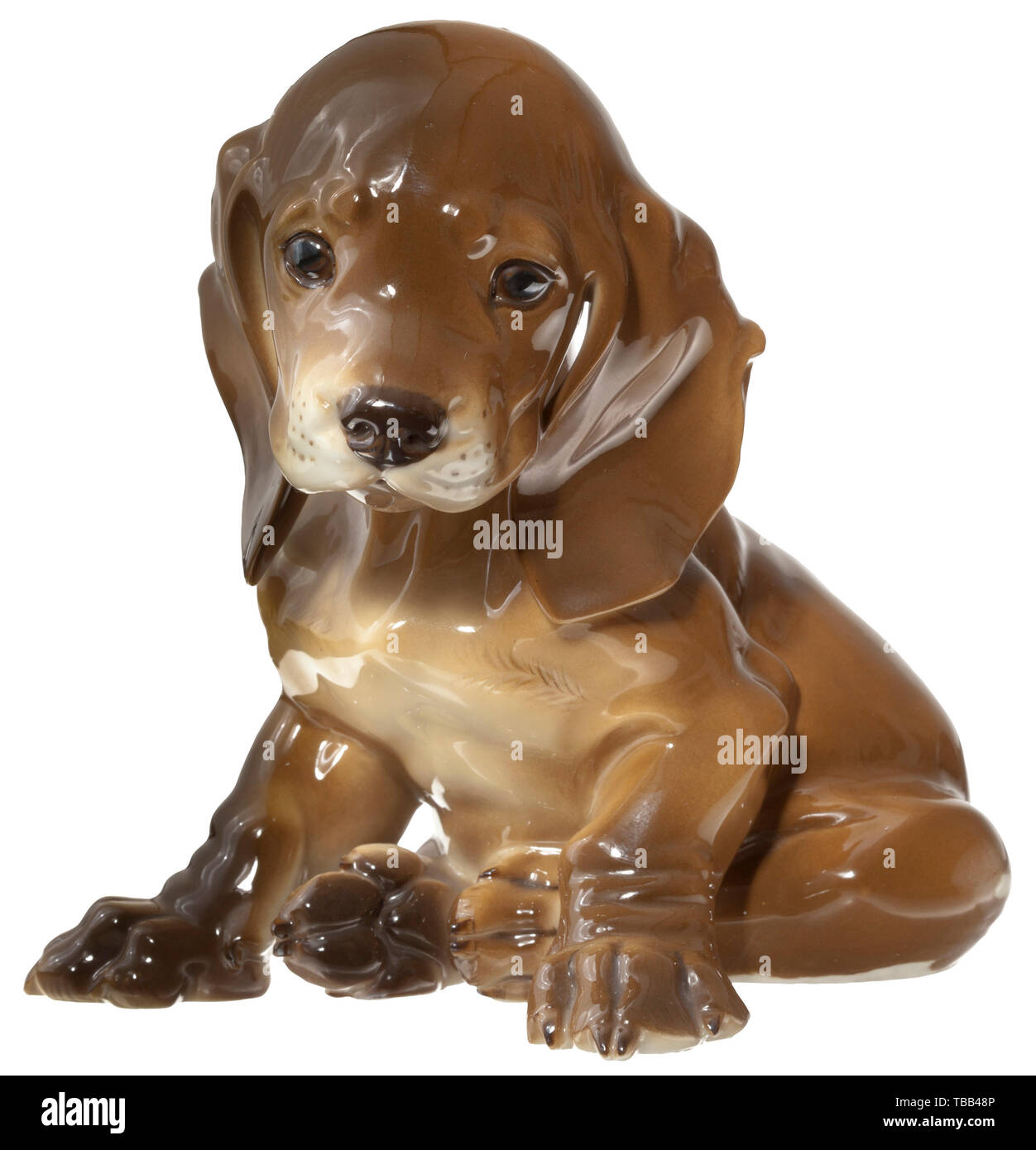 Une séance dachshund puppy en porcelaine polychrome. La partie inférieure avec la signature de l'artiste estampillé 'T. Kärner' et le numéro de modèle '2', vert underglazed fabrication's mark 'SS' Allach dans un octogone. Hauteur 14 cm. Petite puce à la griffe de l'avant-pied droit. Historique rare., historique, porcelaine, faïence, 20e siècle, Editorial-Use-seulement Banque D'Images