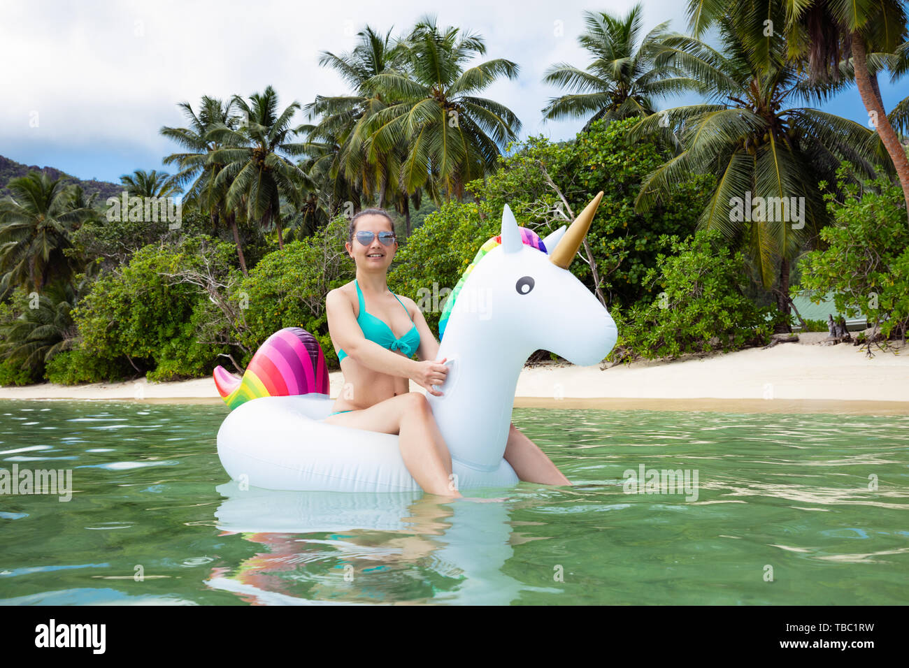 Portrait Of A Smiling Young Woman Sitting on Unicorn gonflable flottant sur la plage à la mer Banque D'Images