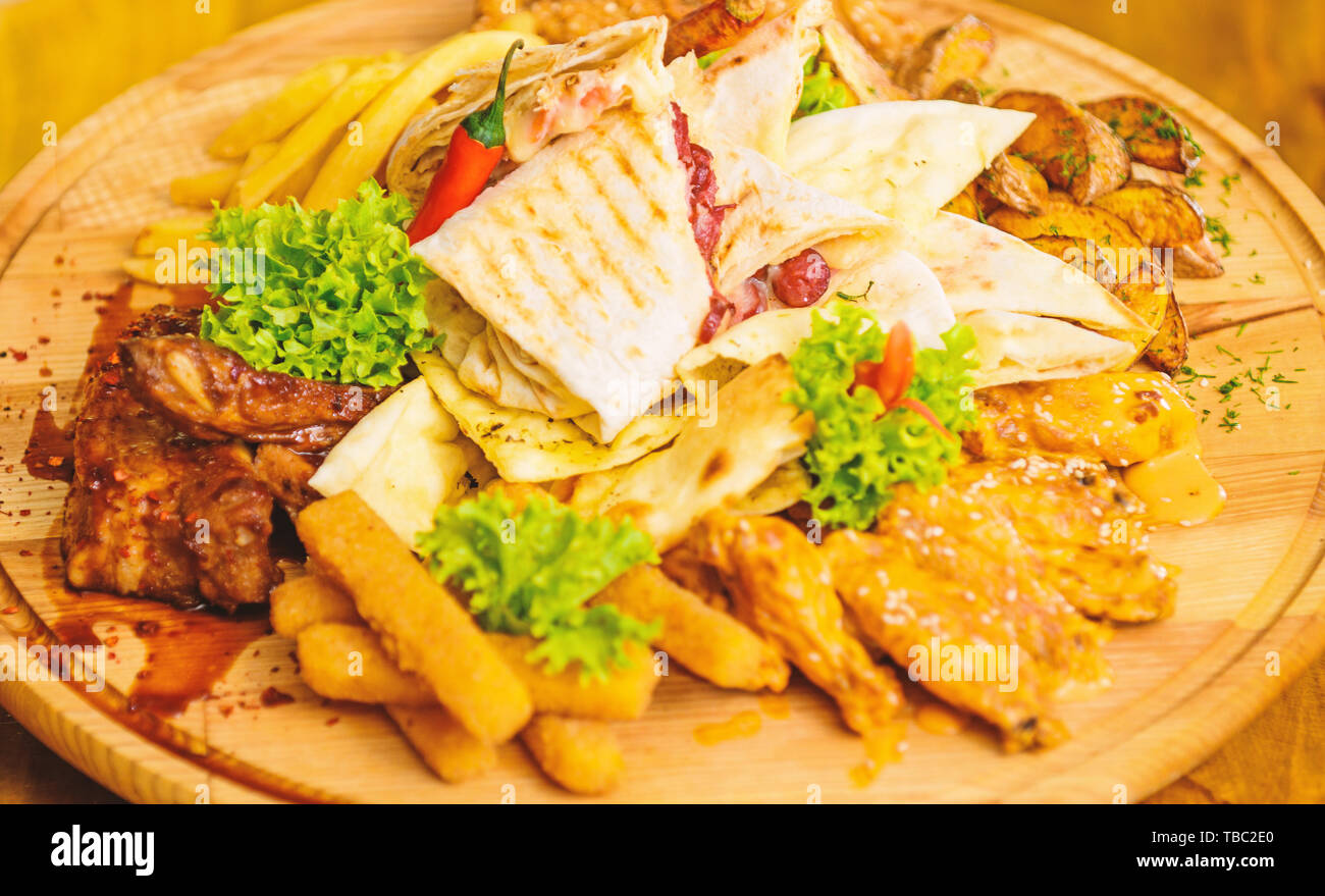Menu snack-bar. Snack de viande pour le groupe d'amis. De délicieux en-cas savoureux. Les repas au restaurant. Snack pour la bière. Planche de bois frites et bâtonnets de poisson viande burrito steak servi avec une salade. Profitez de votre repas. Banque D'Images