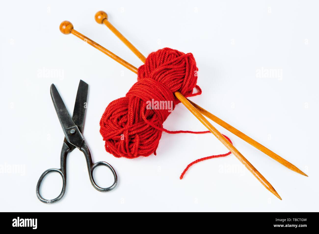 Paire d'aiguilles à tricoter en bois, ciseaux et laine rouge sur fond blanc Banque D'Images