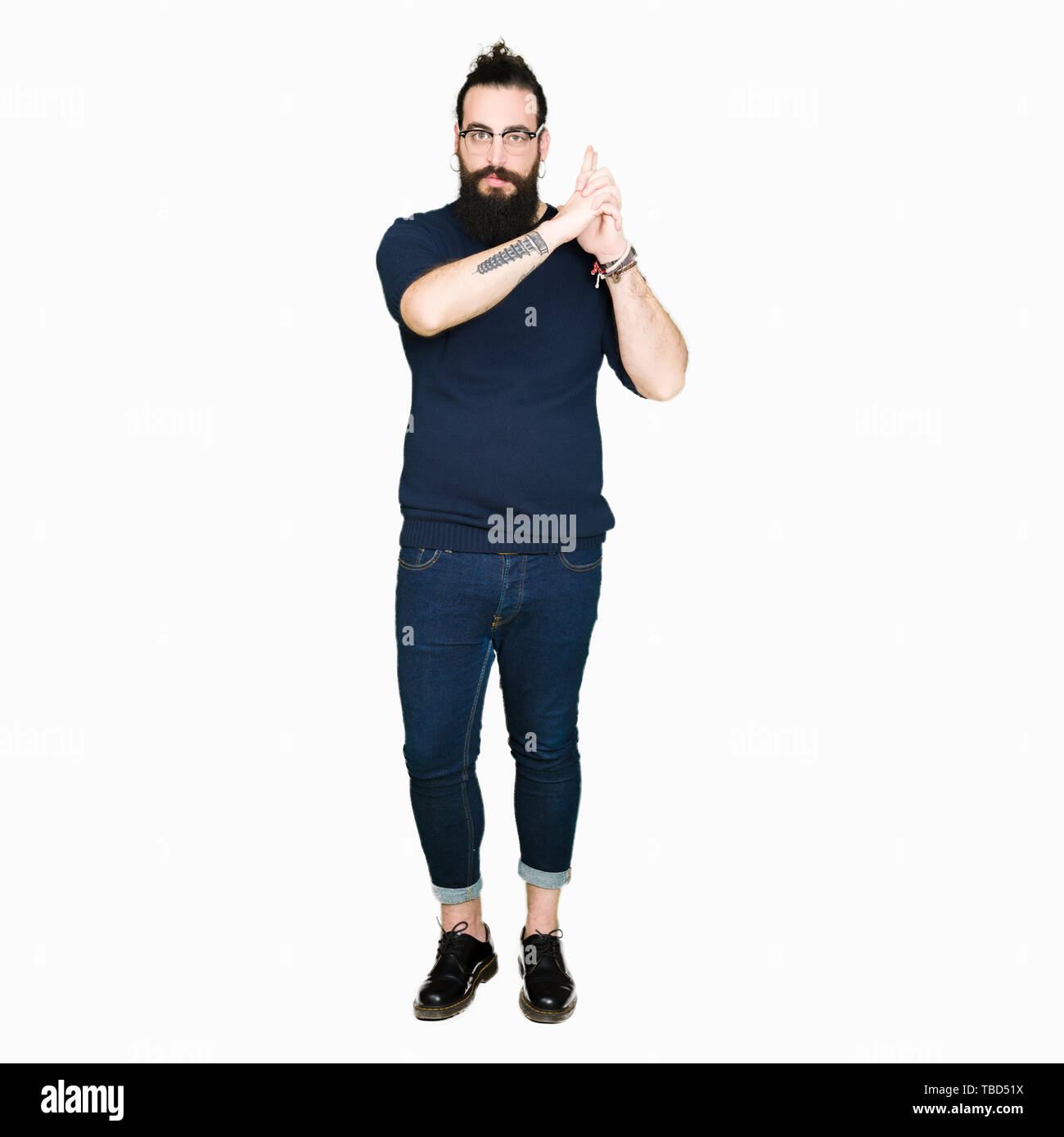 Jeune homme hipster avec de longs cheveux et barbe portant des lunettes Holding gun symbolique avec geste de la main, à l'assassinat d'armes de tir visage en colère, Banque D'Images