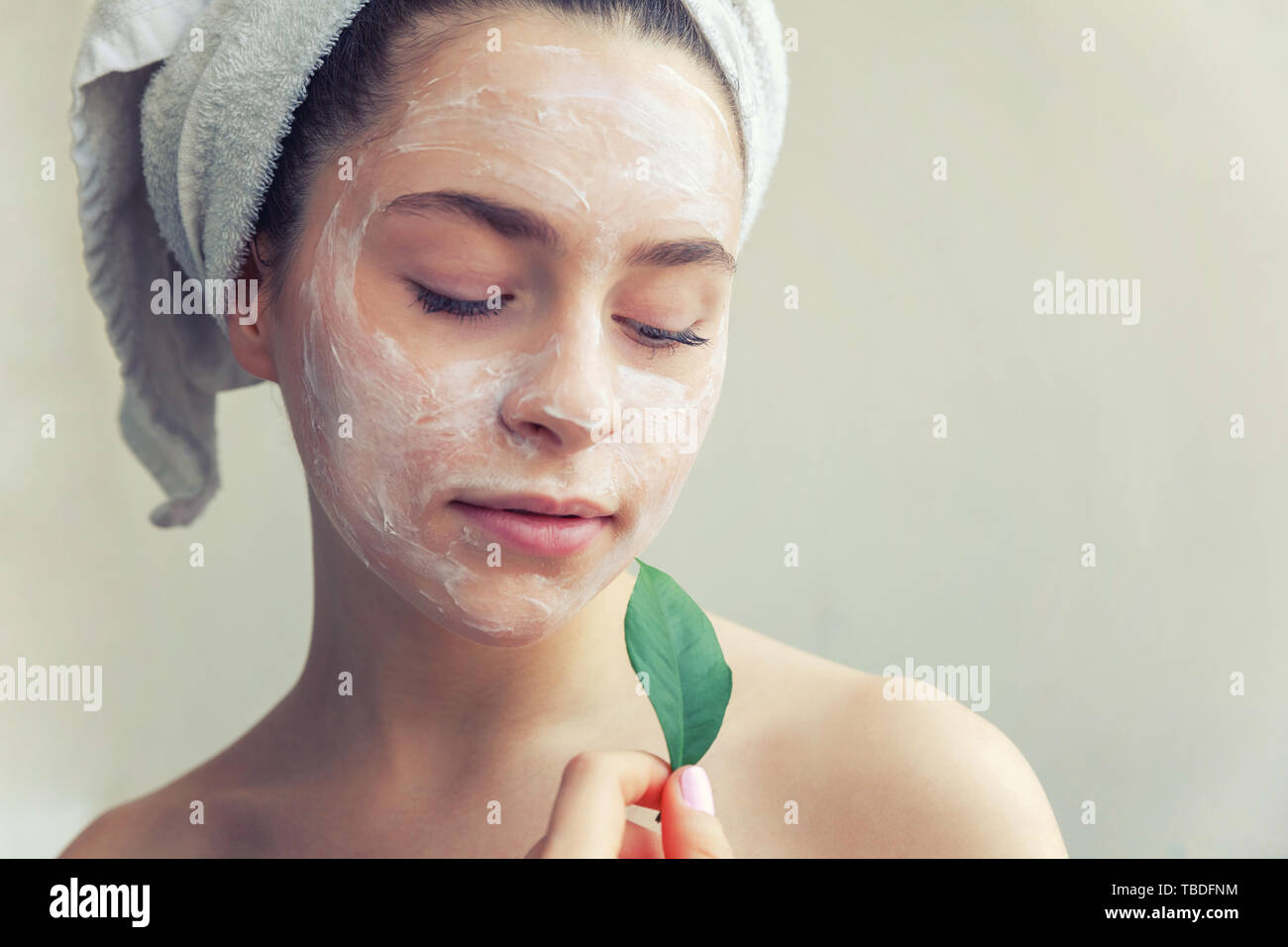 Portrait of woman in towel on head avec blanc masque nourrissant ou la crème sur le visage et le vert feuille dans la main, fond blanc isolé. Clea soin Banque D'Images