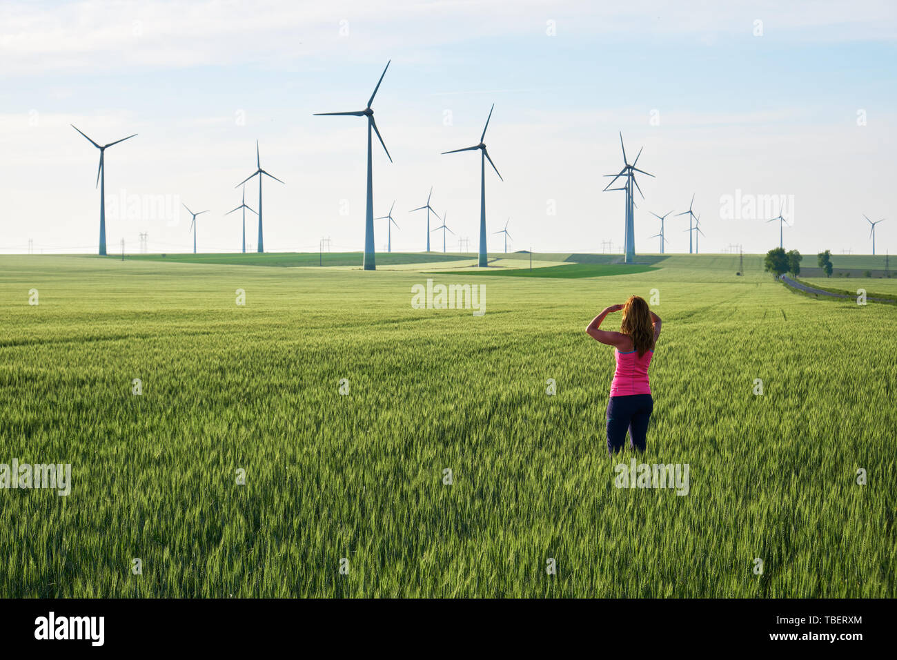 Jeune femme à l'égard des éoliennes au lever du soleil, dans un champ de blé vert. Concept pour les solutions d'énergie durable dans l'avenir. Banque D'Images