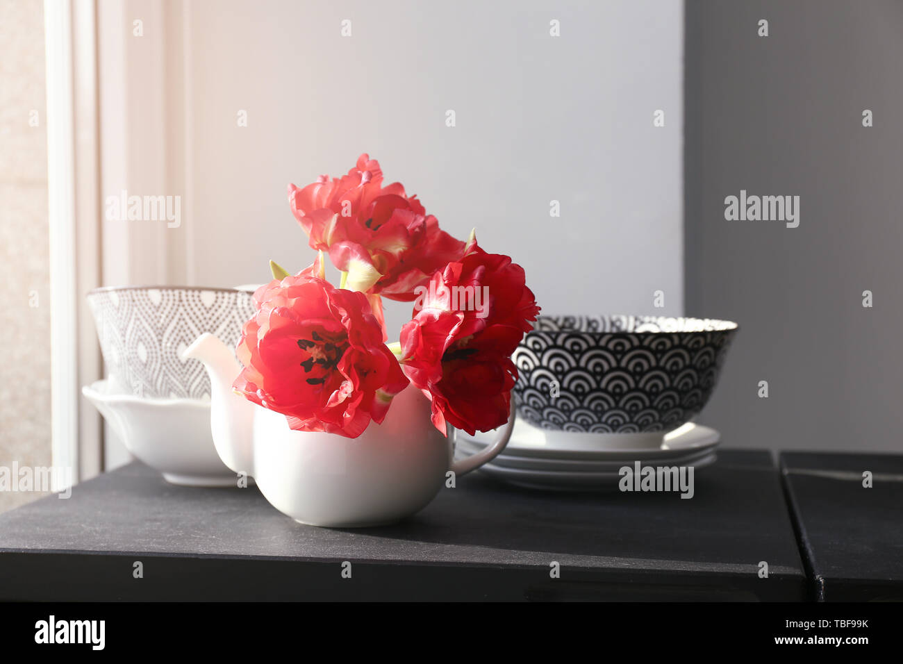 Théière avec de belles fleurs et de la vaisselle sur la table près de window Banque D'Images