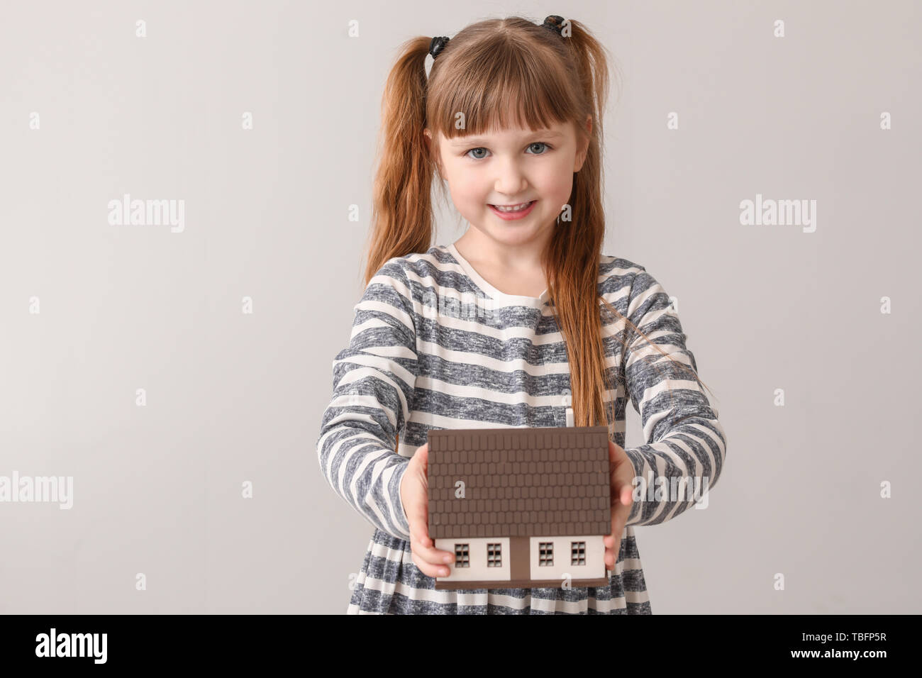 Petite fille avec modèle de maison sur fond clair. Concept de tremblement de terre Banque D'Images