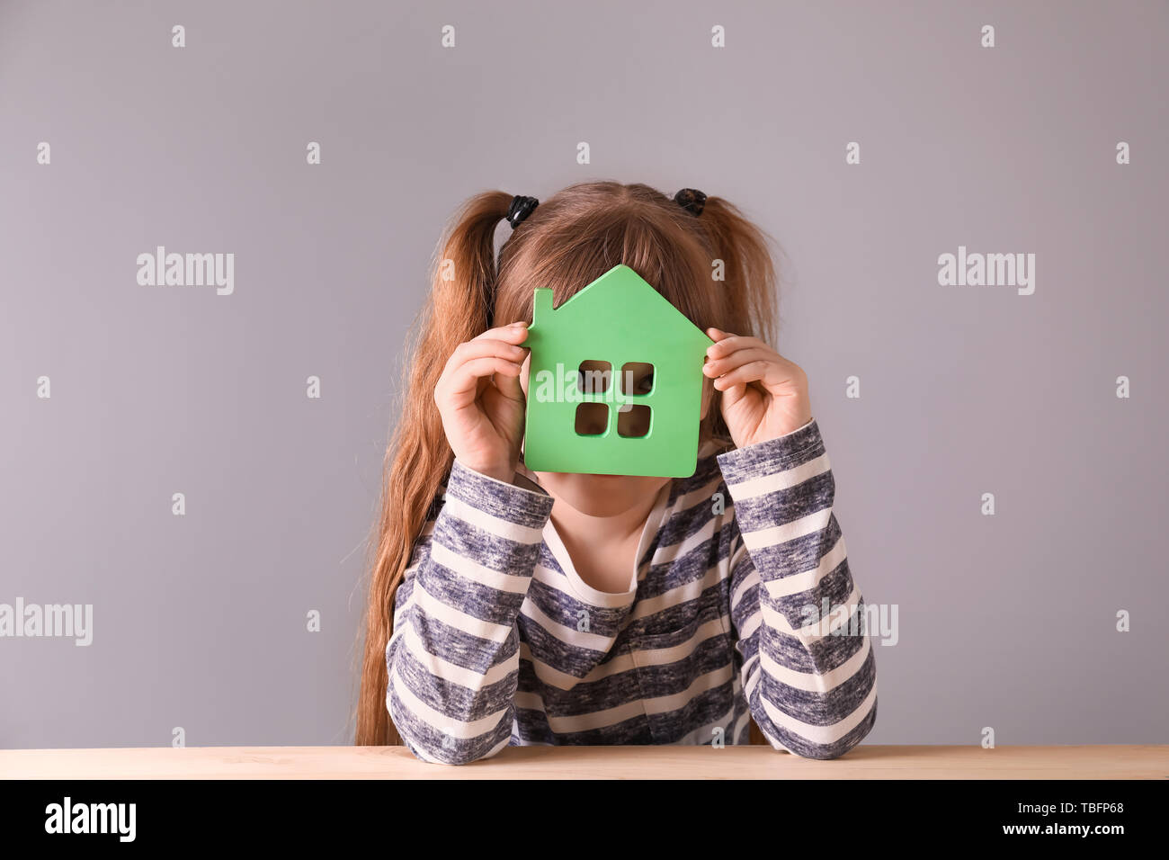 Petite fille avec modèle de maison sur fond gris. Concept de tremblement de terre Banque D'Images