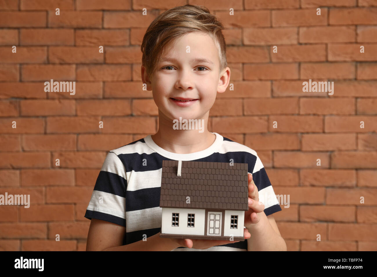 Petit garçon avec modèle de maison sur fond brique. Concept de tremblement de terre Banque D'Images