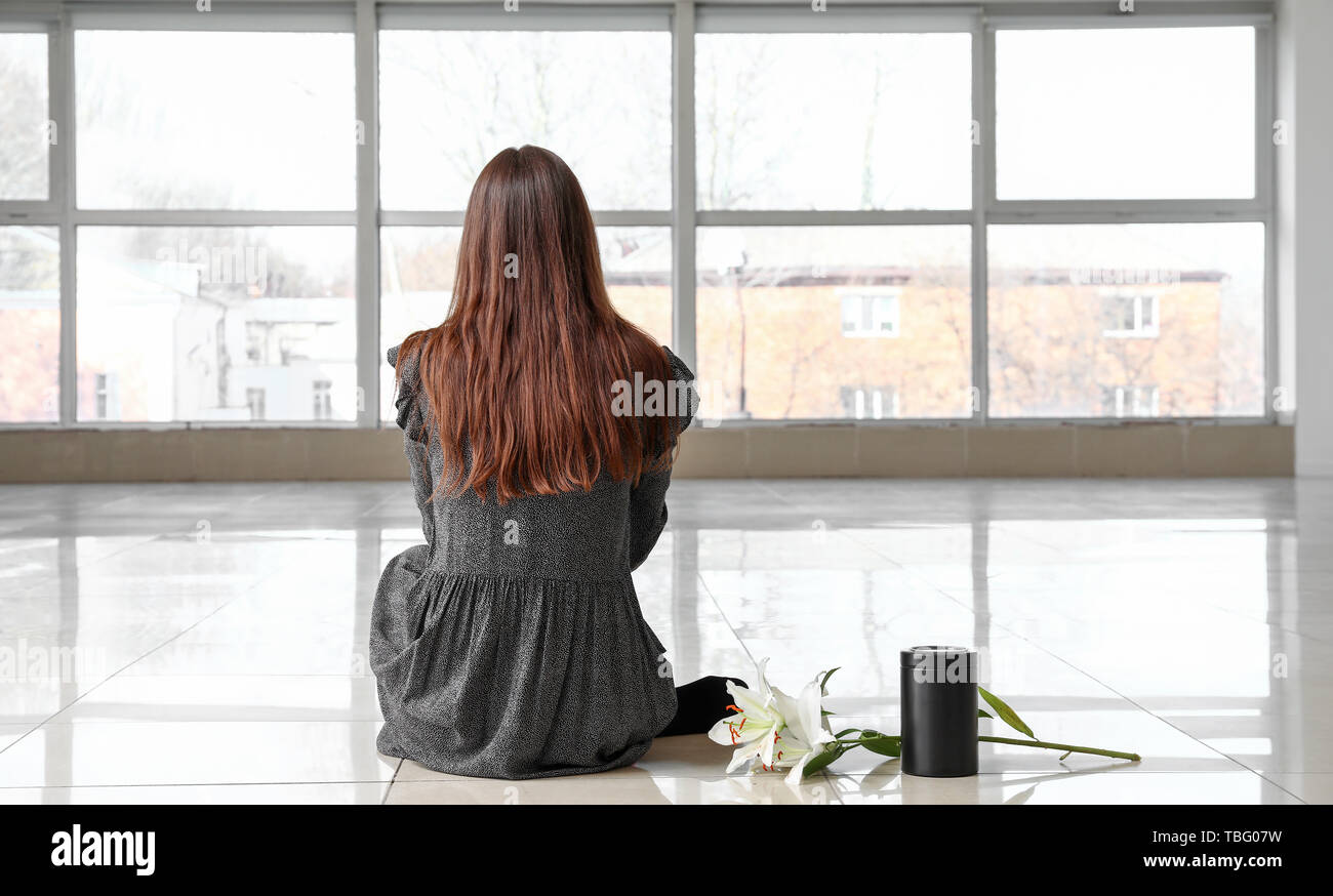 Femme avec des fleurs et de l'urne funéraire lily assis dans la salle vide, vue arrière Banque D'Images