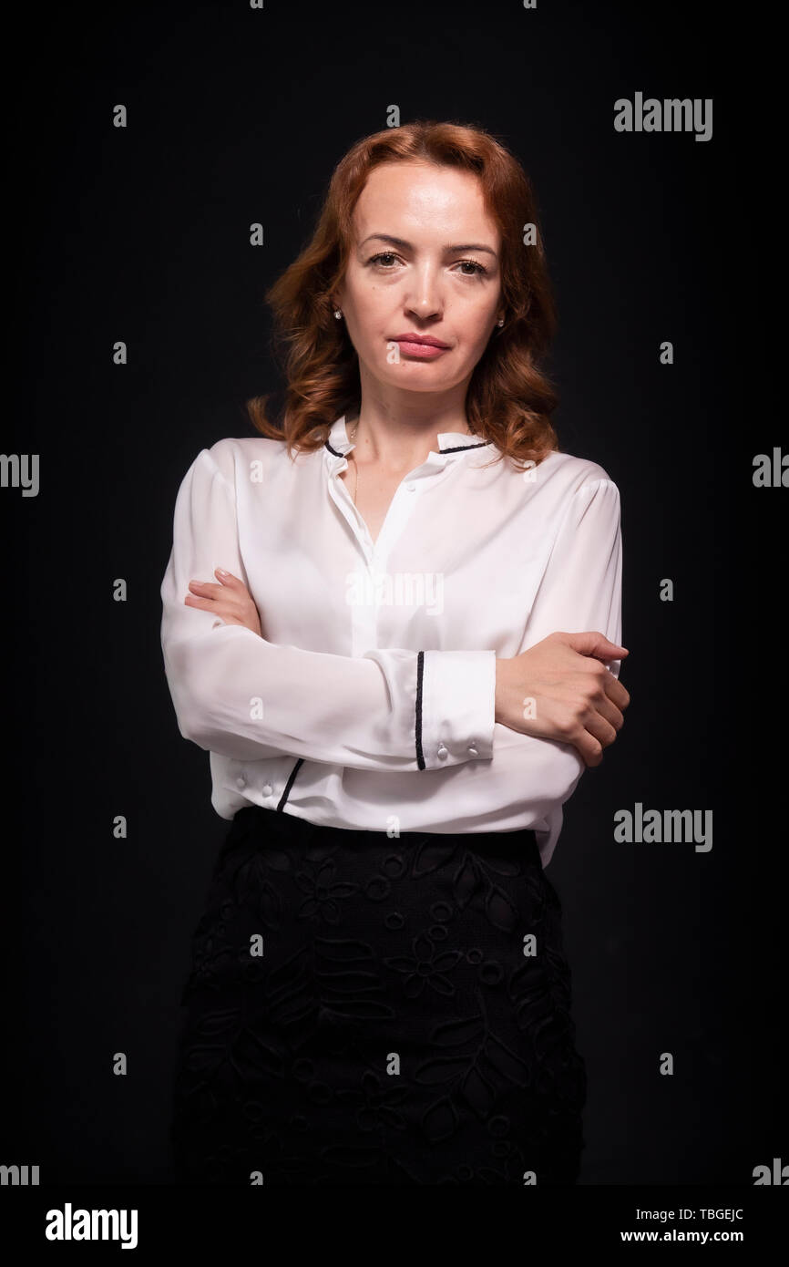 Une femme mature, 45 ans, portrait haut du corps, déterminé et sérieux face à l'expression avec les bras croisés. Le port de jupe chemisier blanc et noir Banque D'Images