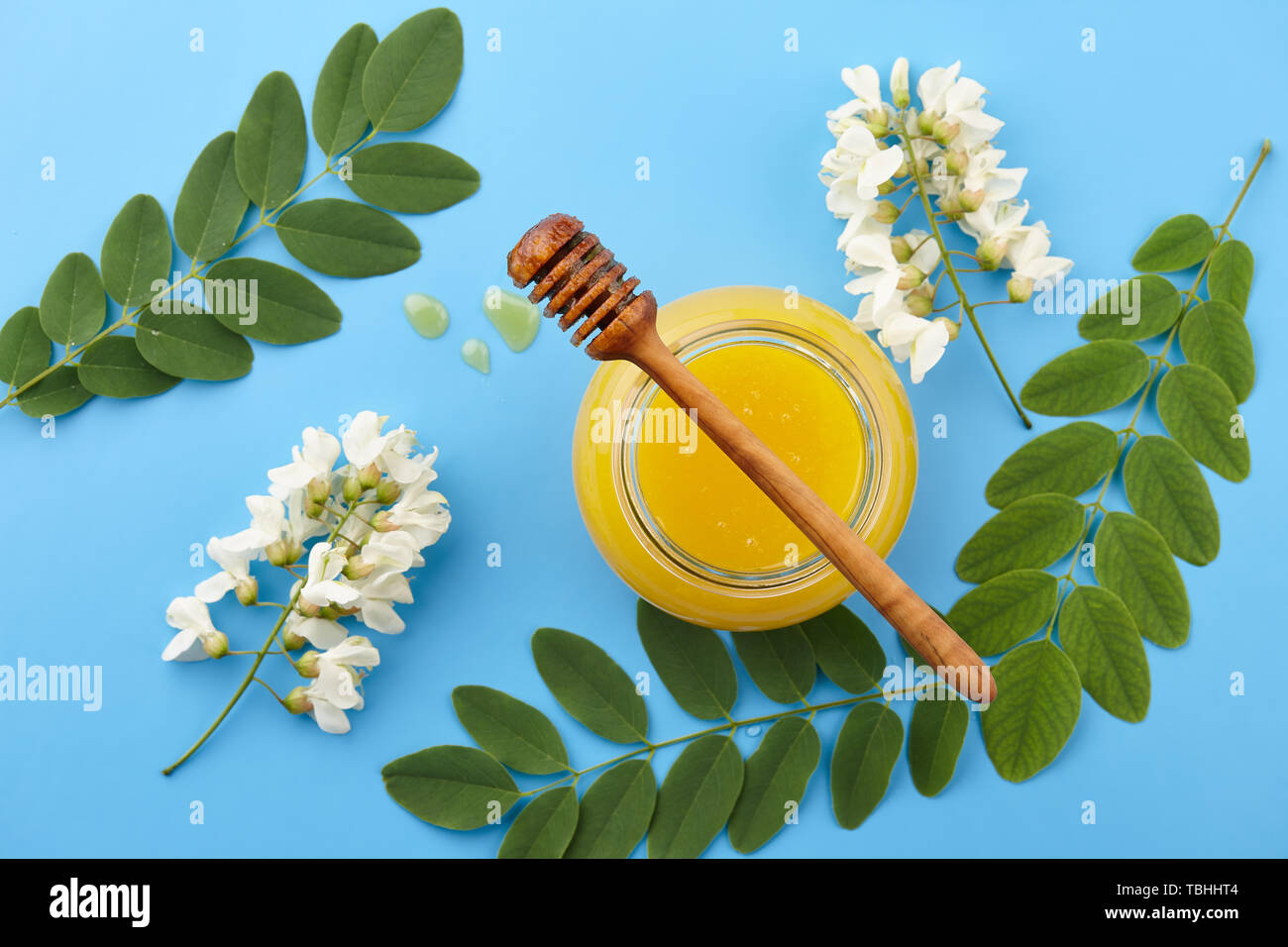 Le miel en pot de verre et d'acacia fleurs sur fond bleu, vue d'en haut Banque D'Images
