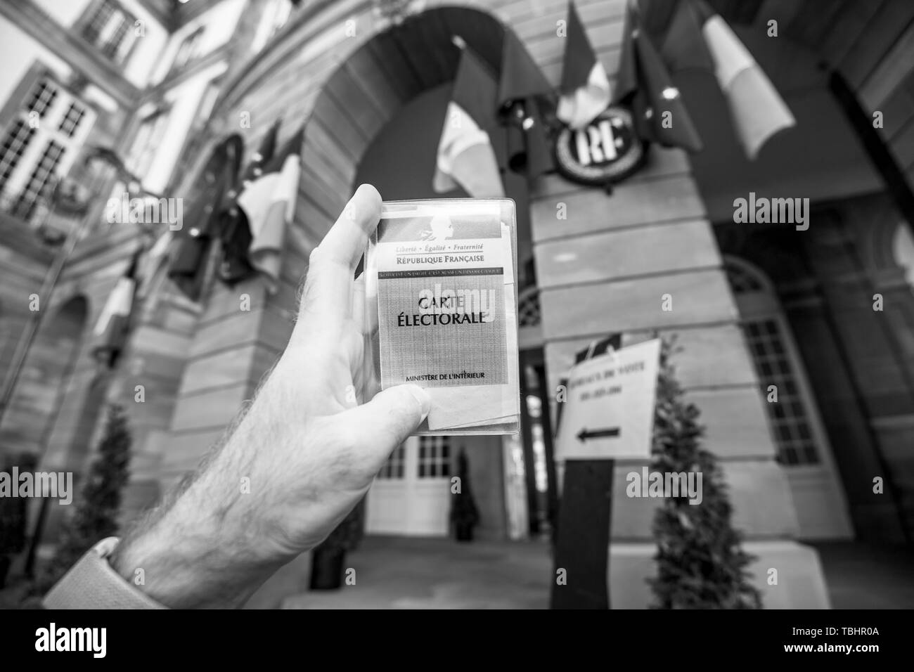 Strasbourg, France - 26 mai 2019 : image de l'homme main tenant l'électeur français voiture Carte Electorale avec l'entrée de l'Hôtel de Ville Hôtel de Ville bureau de vote sur le jour de l'élection du Parlement européen 2019 - noir et blanc Banque D'Images