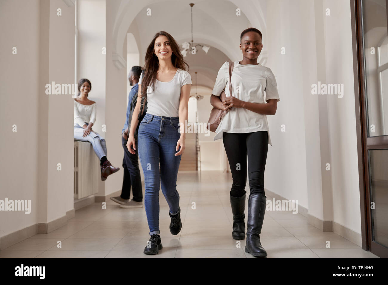 Belles filles élèves Africains de race blanche et marche sur couloir de l'université, aller à la maison après une conférence. Jolies filles se détendre après l'étude, happy smiling. Concept de l'université. Banque D'Images