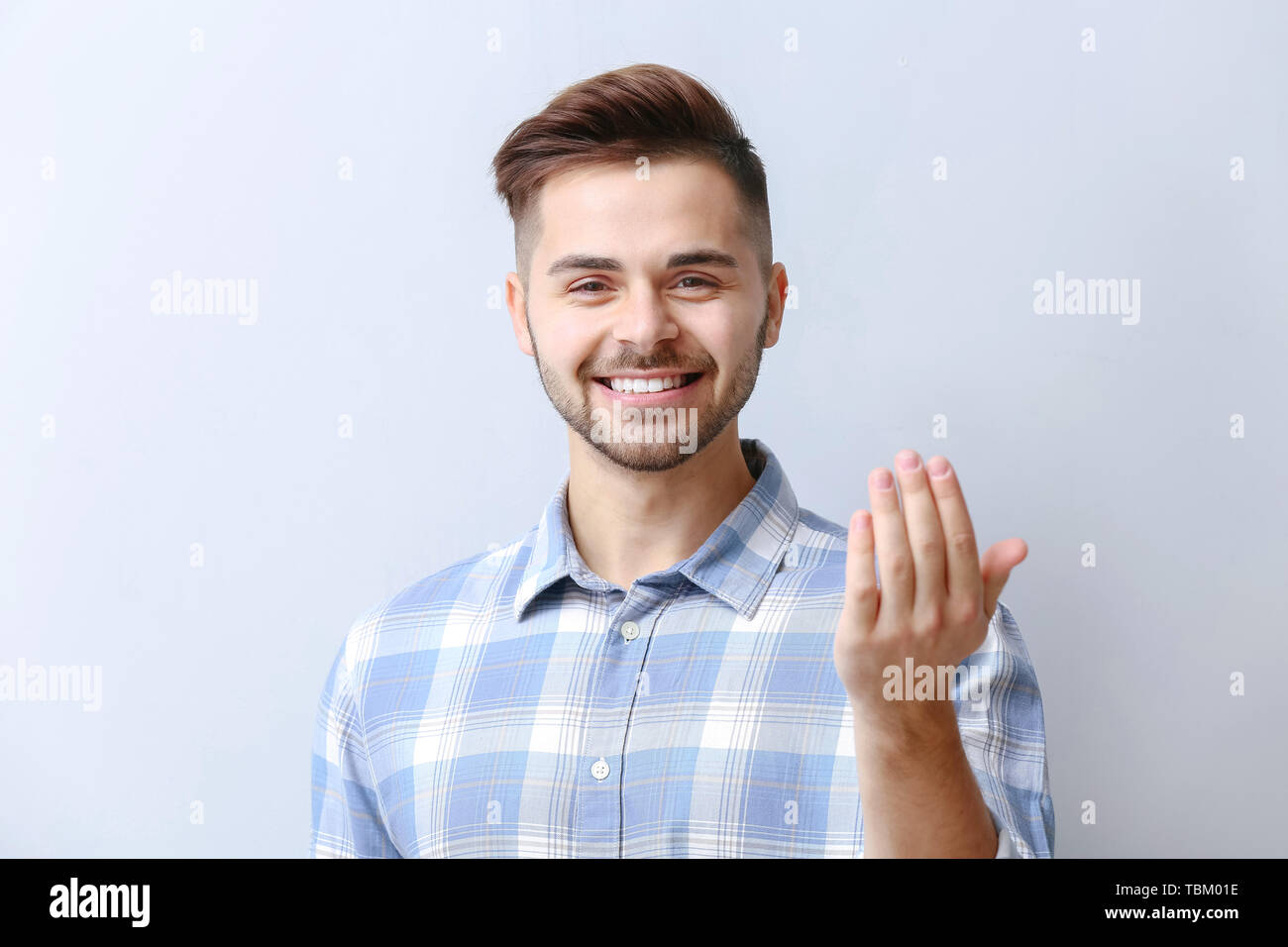 Bel homme montrant "viens ici" geste sur fond clair Banque D'Images
