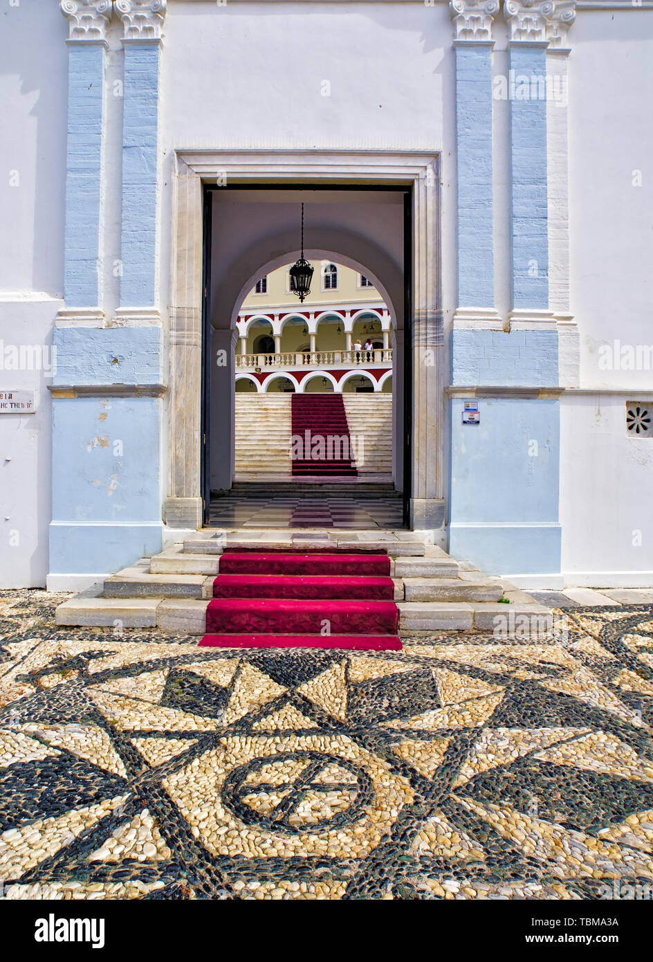 L'Église chrétienne orthodoxe de la Vierge Marie à l'ile de Tinos, Grèce, noir et blanc cailloux marbre, entrée principale, escalier avec tapis rouge. Banque D'Images
