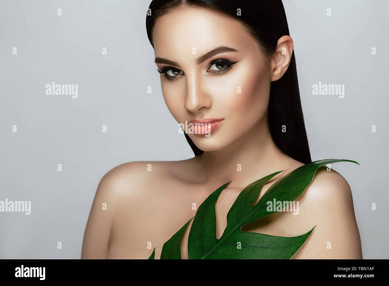 Belle femme visage avec le maquillage parfait et une peau saine avec des feuilles tropicales soins visage beauté. Banque D'Images