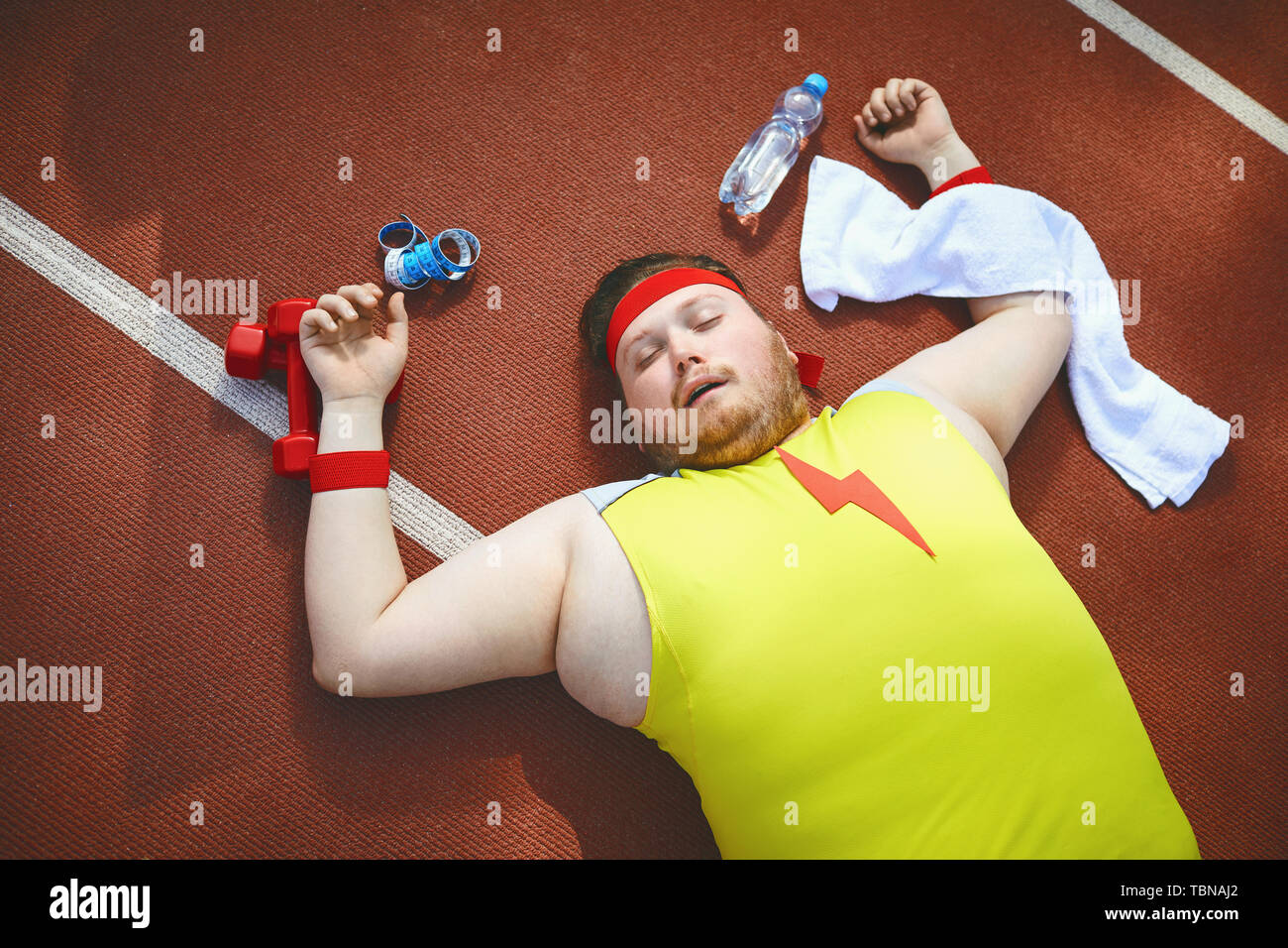 Fat lazy man sleeps fatigué se trouve sur la piste dans le stade. La notion de perte de poids, le régime alimentaire. Vue d'en haut. Banque D'Images