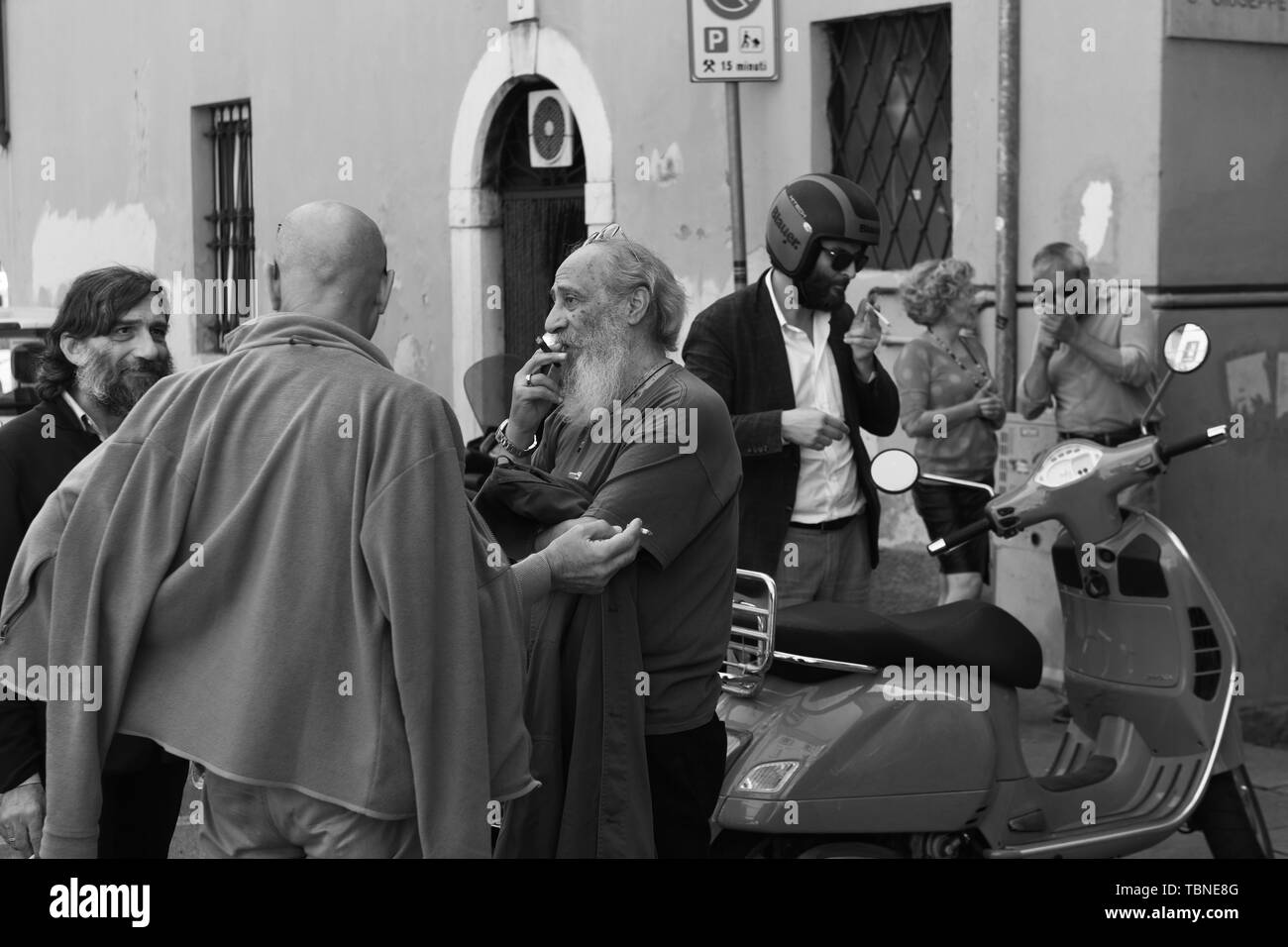 Rassemblement d'hommes parlant italien et le tabagisme dans les rues de Brescia Italie Banque D'Images