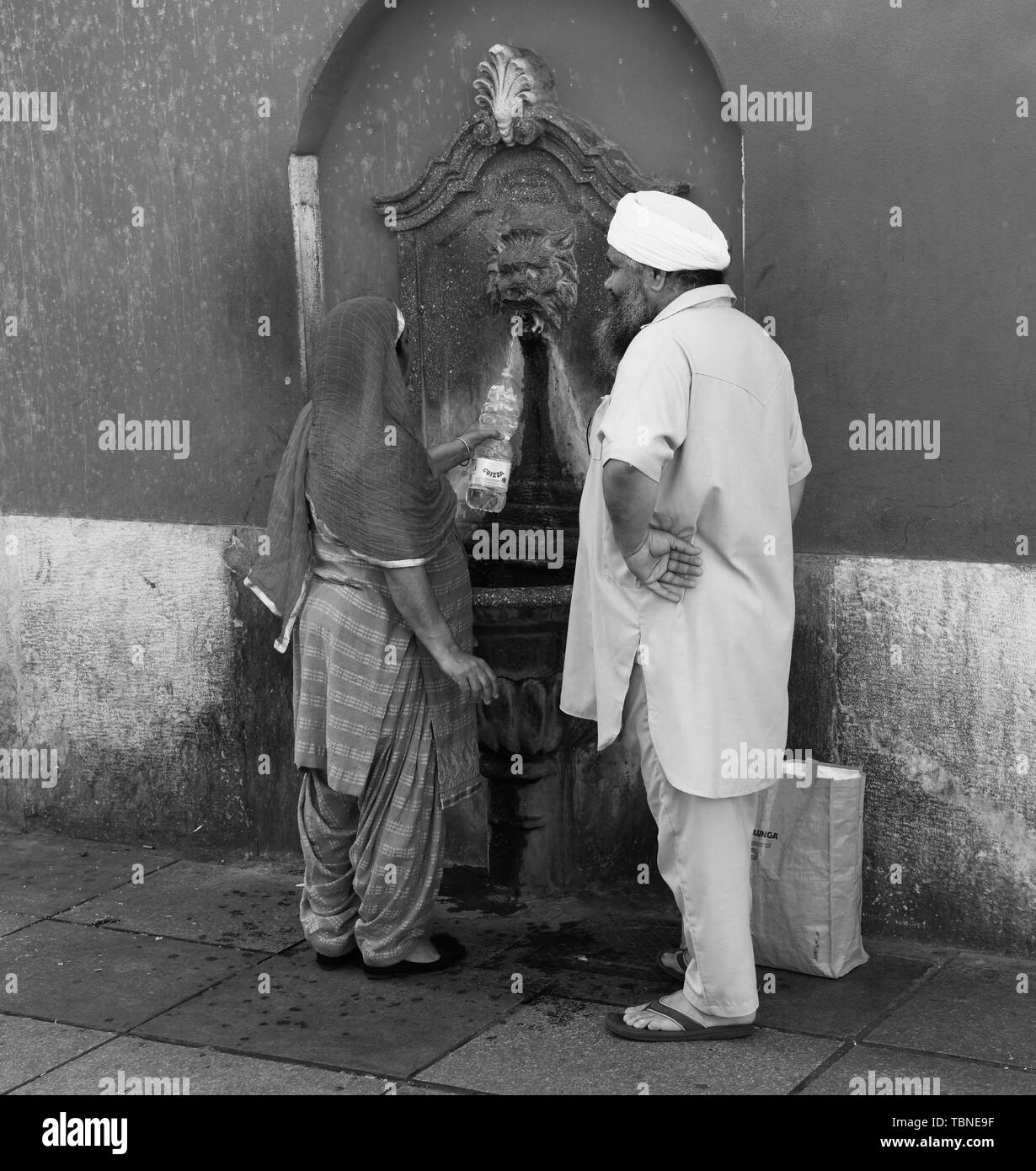 Asian couple remplir bouteille d'eau en plastique d'une fontaine d'eau publique à Brescia Italie Banque D'Images