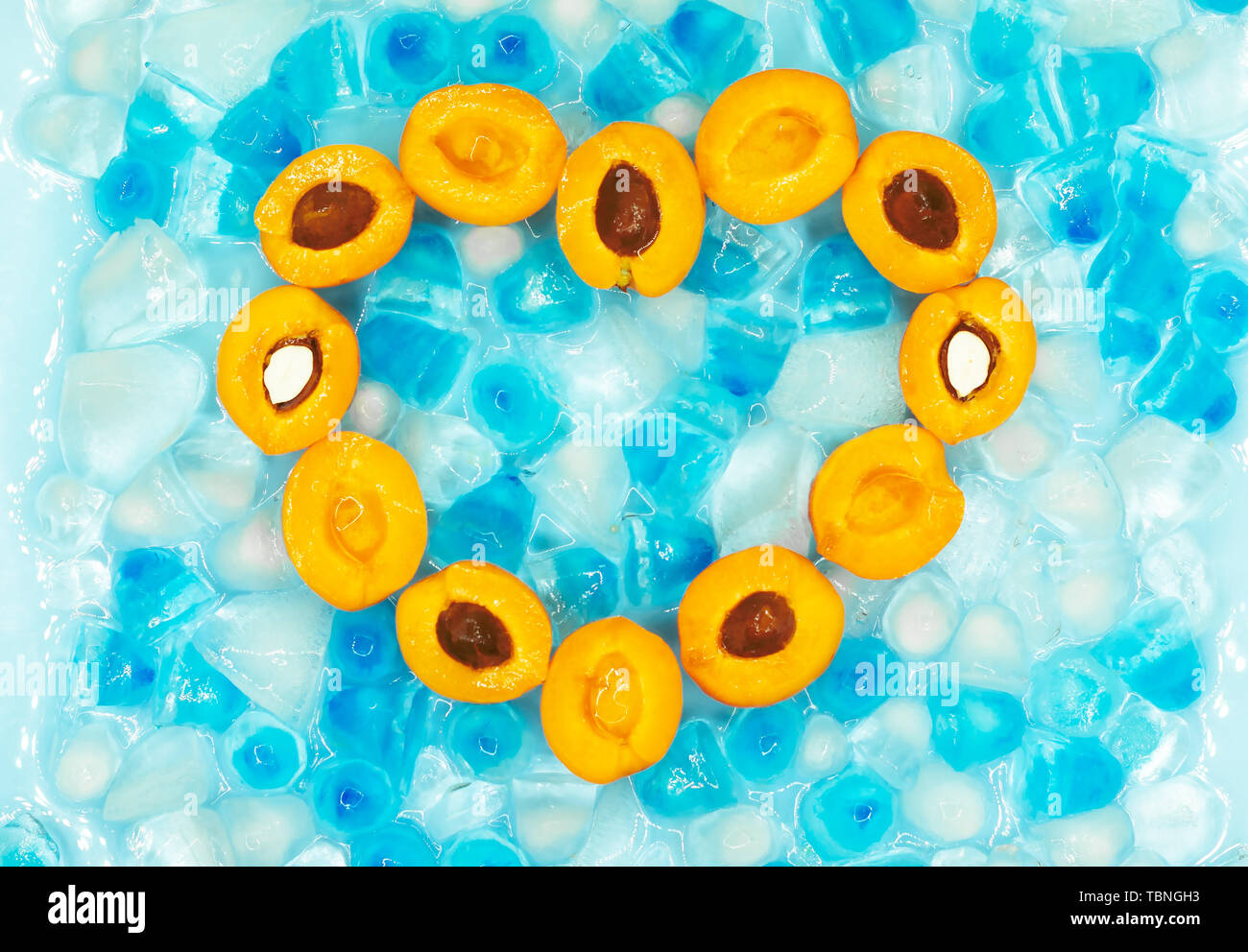 Coeur en abricots mûrs avec ou sans pierres dans le contexte de transparence et de bleu des glaçons avec copie espace. Vue d'en haut. Les fruits frais. S Banque D'Images