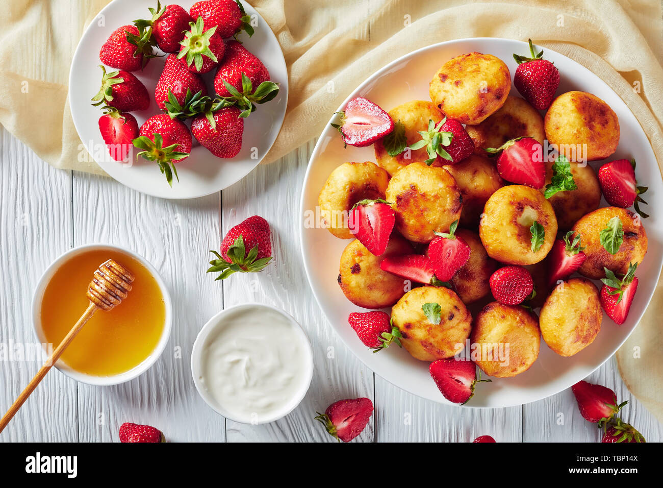 Vue de dessus de fromage cottage avec crêpes aux fraises sur une plaque blanche sur une table en bois avec du miel, de la crème sure et de fraises fraîches dans Banque D'Images