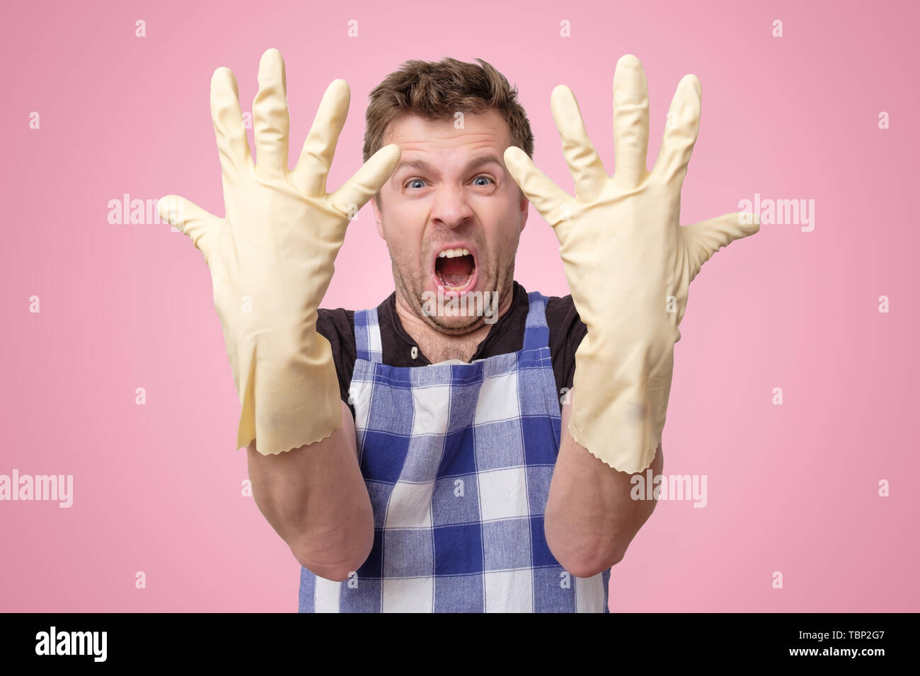 L'homme mature avec des gants de caoutchouc est fatigué et ennuyé par les tâches ménagères Banque D'Images