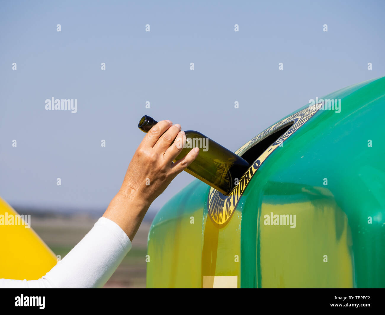 Une femme mature tirant une bouteille de cristal dans un bac vert de recyclage verre avec le texte espagnol "seulement les contenants de verre' Banque D'Images
