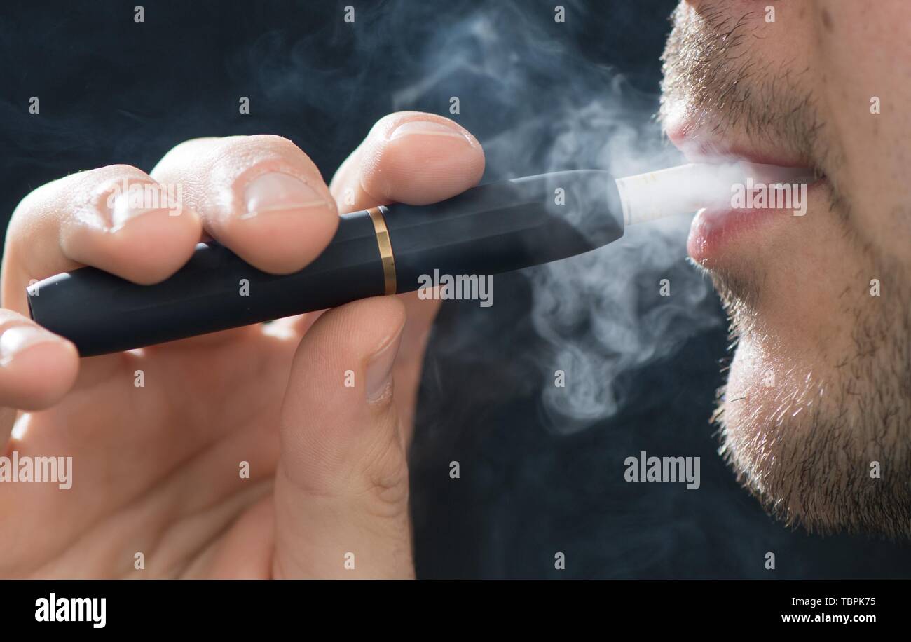 31 mai 2019, Saxe, Dresde : Un homme fume avec le réchauffeur de tabac électroniques IQOS (J'arrête de fumer ordinaire) de la compagnie de tabac Philip Morris. Le bâtonnet de tabac ne doit pas être confondu avec une e-cigarette. Parce que contrairement à celui-ci, qui est rempli de soi-disant liquides, iQOS contient encore du tabac. La différence est que le tabac n'est pas brûlé, mais seulement du chauffage. Les consommateurs en Allemagne ont acheté moins de cigarettes de manière significative l'année dernière qu'en 2017. Au lieu de cela, ils se sont tournés davantage vers le tabac et 'produits de prochaine génération telles que les e-cigarettes et tabac. Photo : Sebastian Ka Banque D'Images