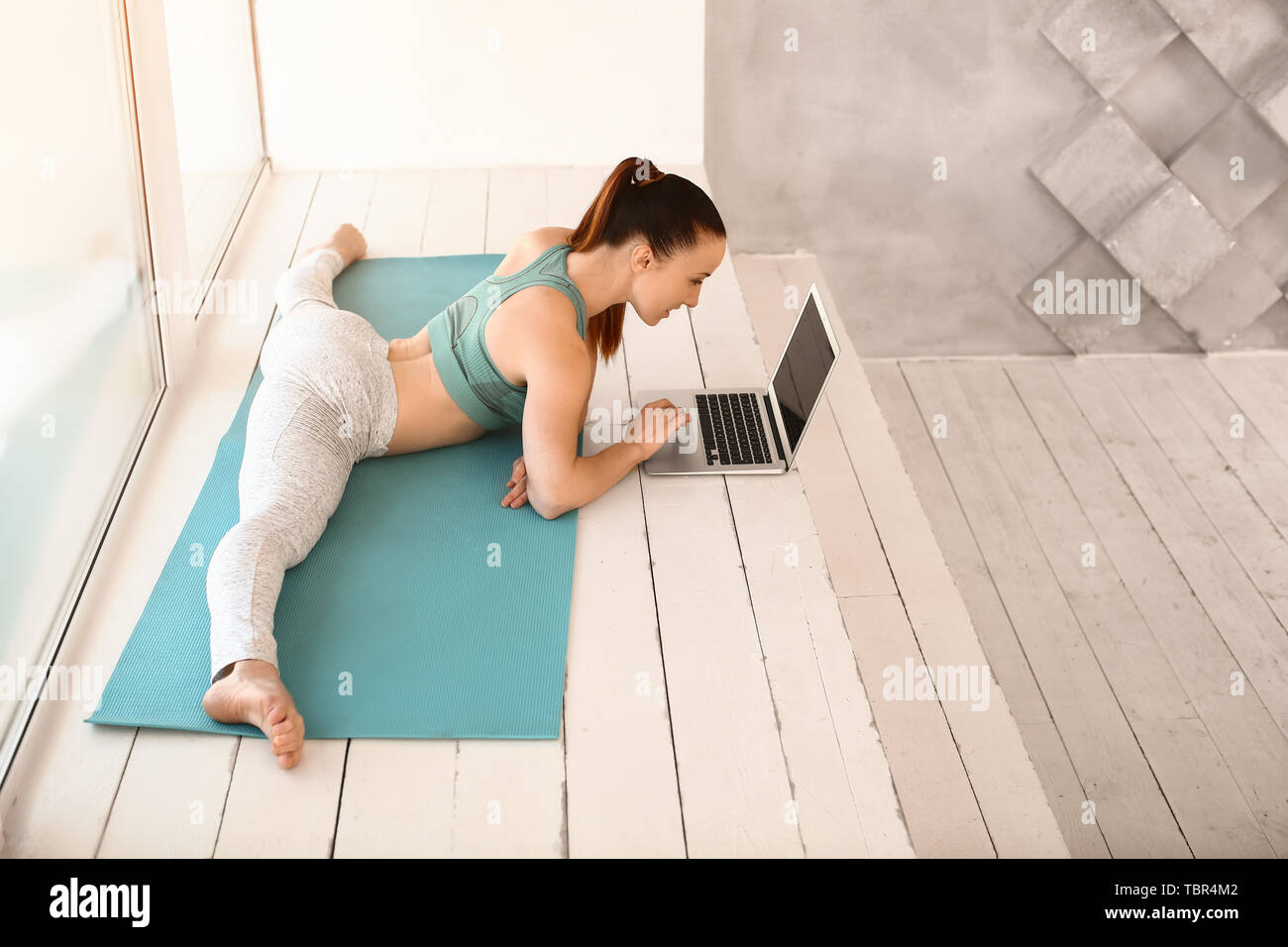 Sporty young woman with laptop faisant leg-split in gym Banque D'Images