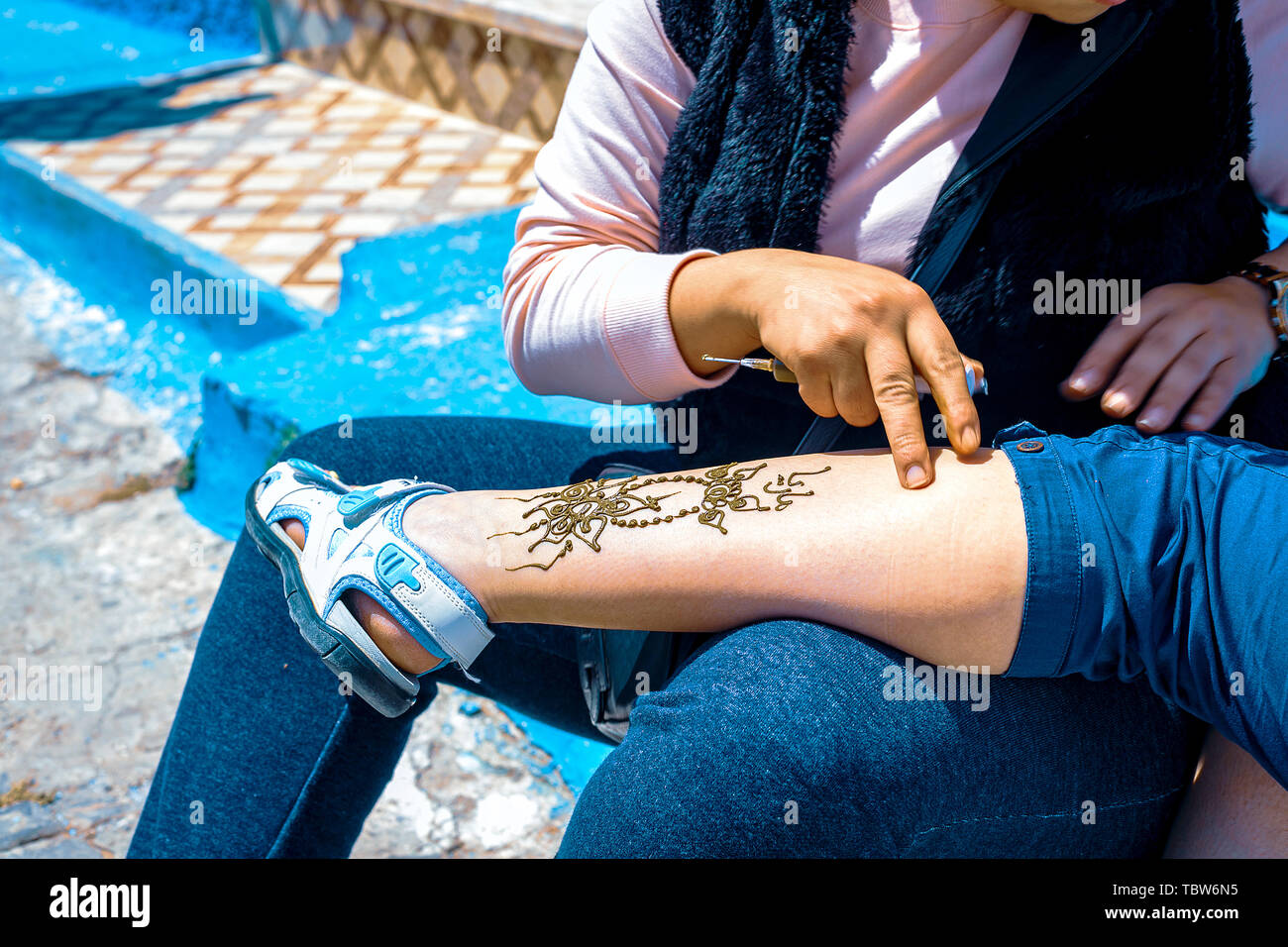 L'application de l'artiste tatouage au henné sur les femmes jambe dans les rues de Marrakech, Maroc, Afrique Banque D'Images