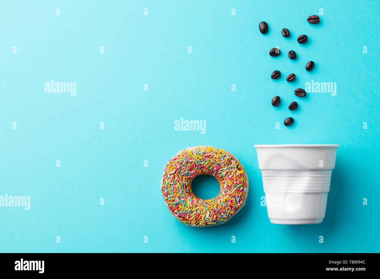 Donut avec blanc tasse de haricots et les grains de café sur fond bleu. Copier l'espace. Banque D'Images