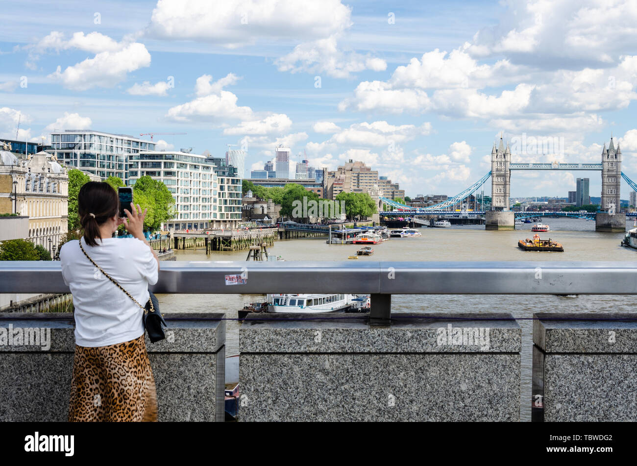 Une dame sur le pont de Londres prend une photographie de Tower Bridge à la Tamise en utilisant son téléphone mobile. Banque D'Images