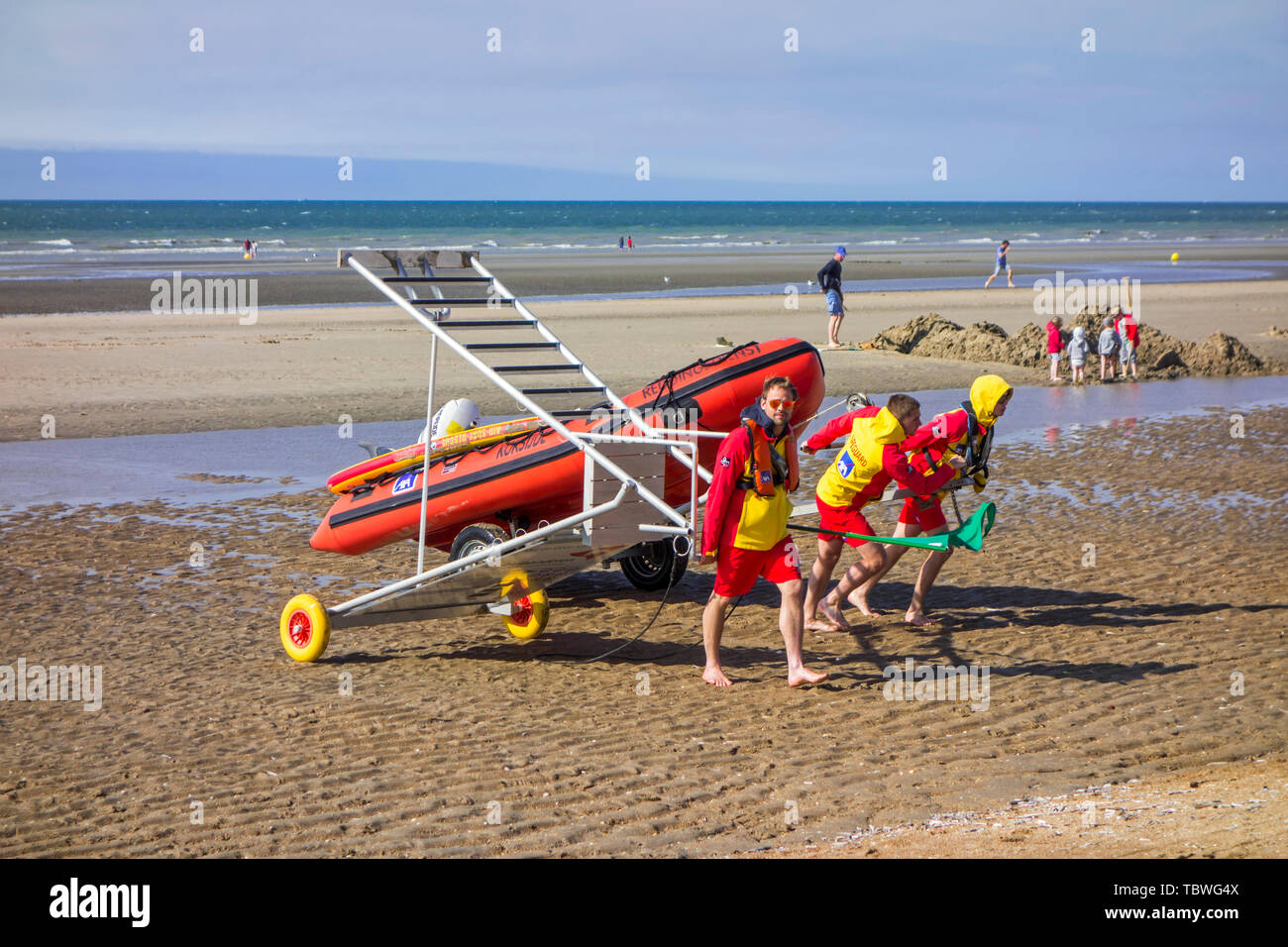 Trois sauveteurs de plage bateau de sauvetage gonflable tirant et chaise haute portable / tower retour à la base le long de la côte de la mer du Nord en Belgique, Belgique Banque D'Images