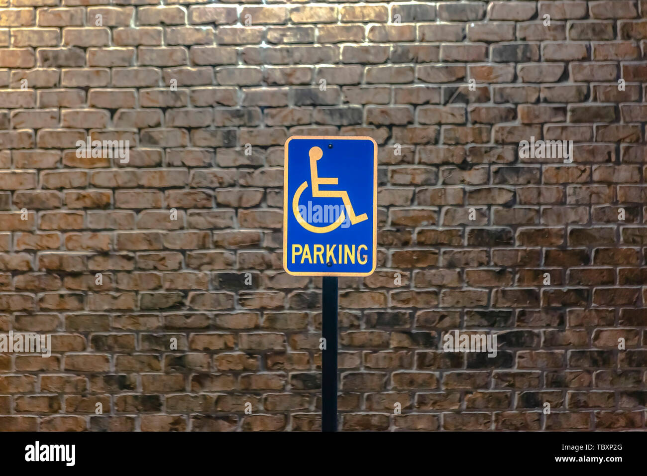 Handicap parking sign contre un mur en brique de pierre illuminée par la lumière du soleil Banque D'Images