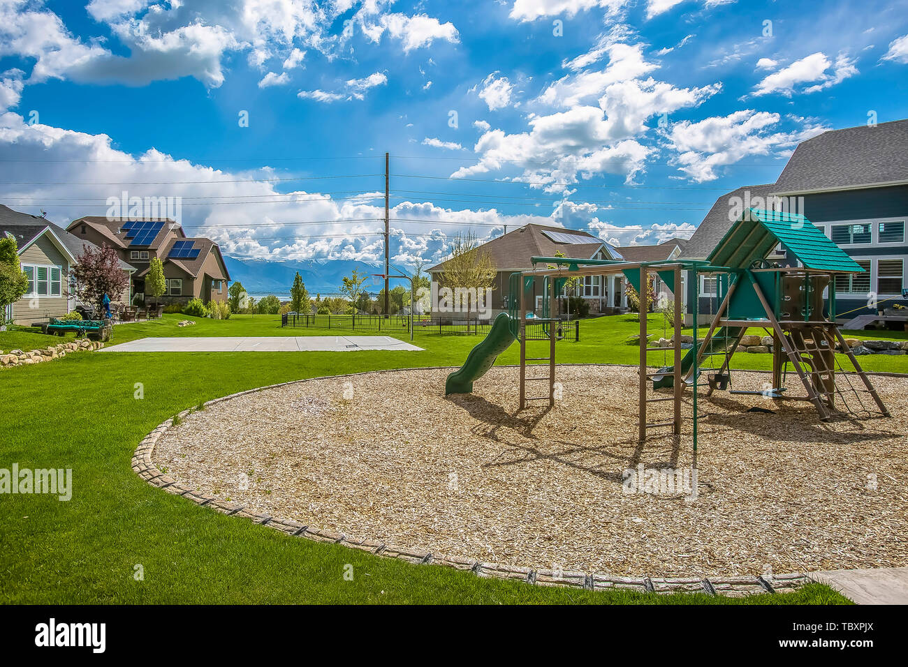 Jeux pour enfants sur un riche domaine vert entouré d'arbres et maisons Banque D'Images Jeux pour enfants sur un riche domaine vert entouré d'arbres et maisons Banque D'Images