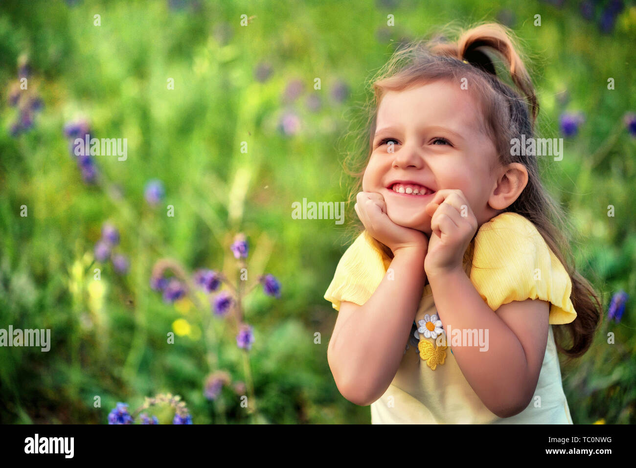 Jolie petite fille souriante à l'extérieur dans le champ vert. Portrait de l'enfant Banque D'Images