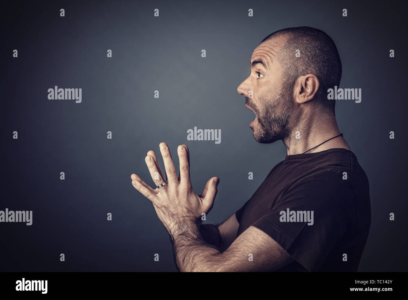 Studio portrait de l'homme aux cheveux courts et à l'expression surprise de la barbe et les mains croisées devant lui. Vu de profil. Banque D'Images