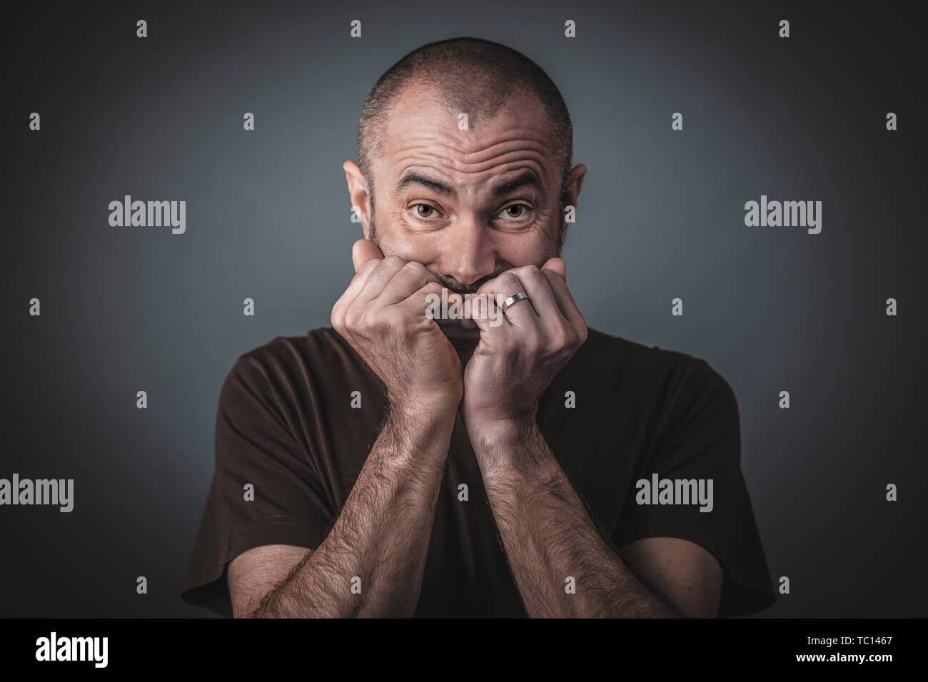Portrait de l'homme effrayé avec les mains jointes près de la bouche. Cheveux courts et la barbe, des vêtements décontractés. Banque D'Images