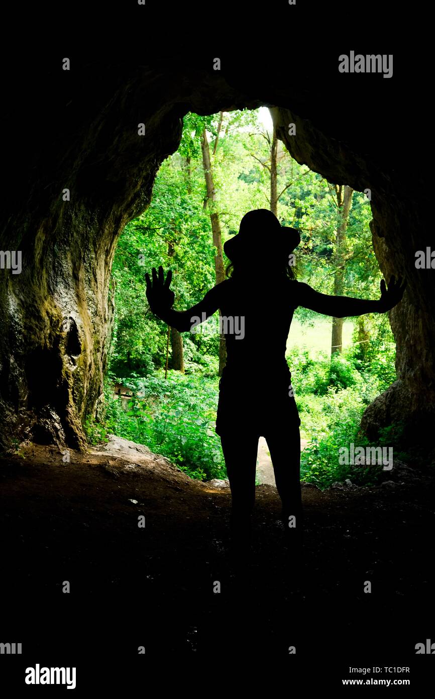 Fille mince silhouette à l'entrée de grotte naturelle dans la forêt, les jeunes explorer Banque D'Images