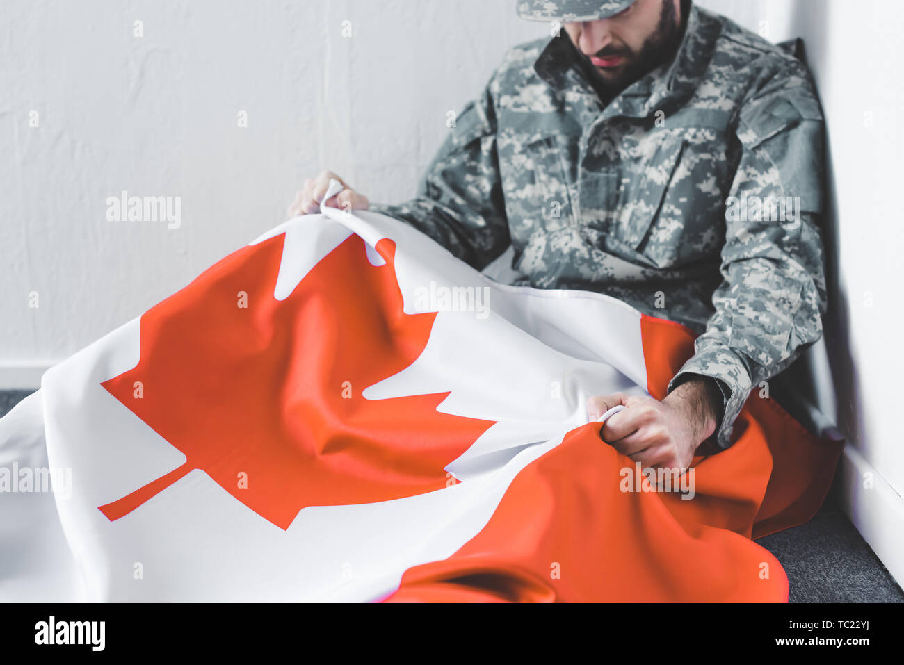 L'homme déprimé en uniforme militaire assis sur le plancher en coin et tenant le drapeau national du canada Banque D'Images