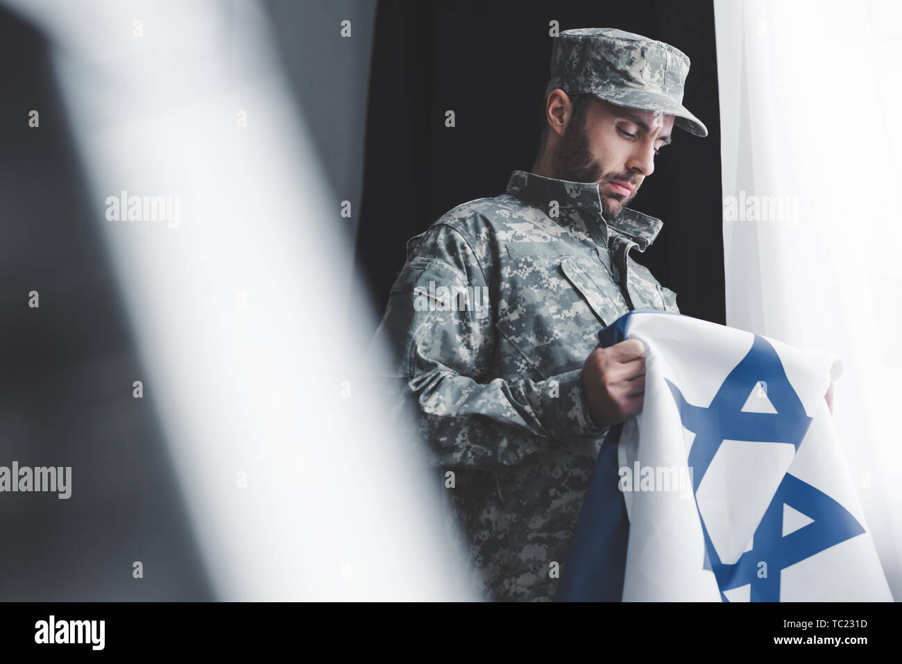 Portrait d'homme en uniforme militaire holding Israël drapeau national en position debout par fenêtre Banque D'Images