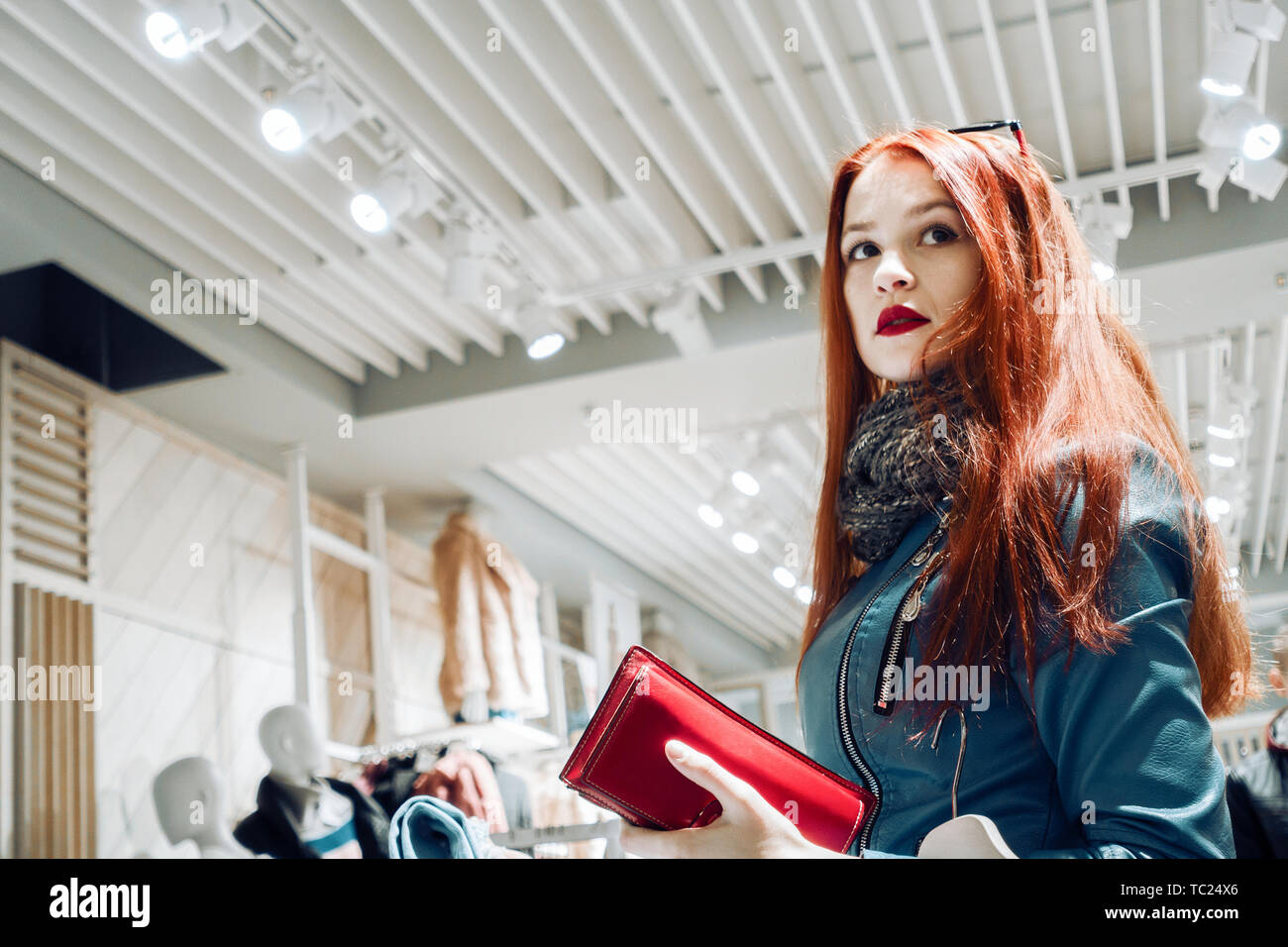 Portrait de jeune fille à cheveux rouge veste en cuir bleu. femme en boutique avec votre portefeuille dans les mains Banque D'Images